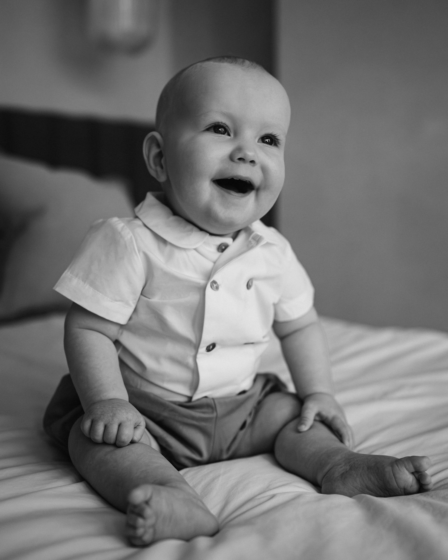Black and white series showing a baby in formal wear sitting on a bed.