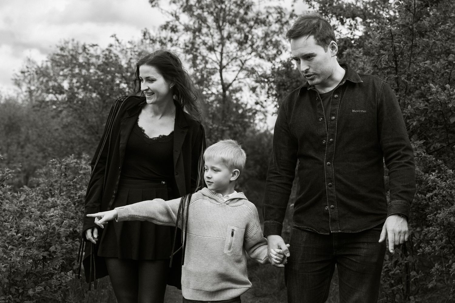 Black and white photo of a family with young boy walking outdoors among trees.