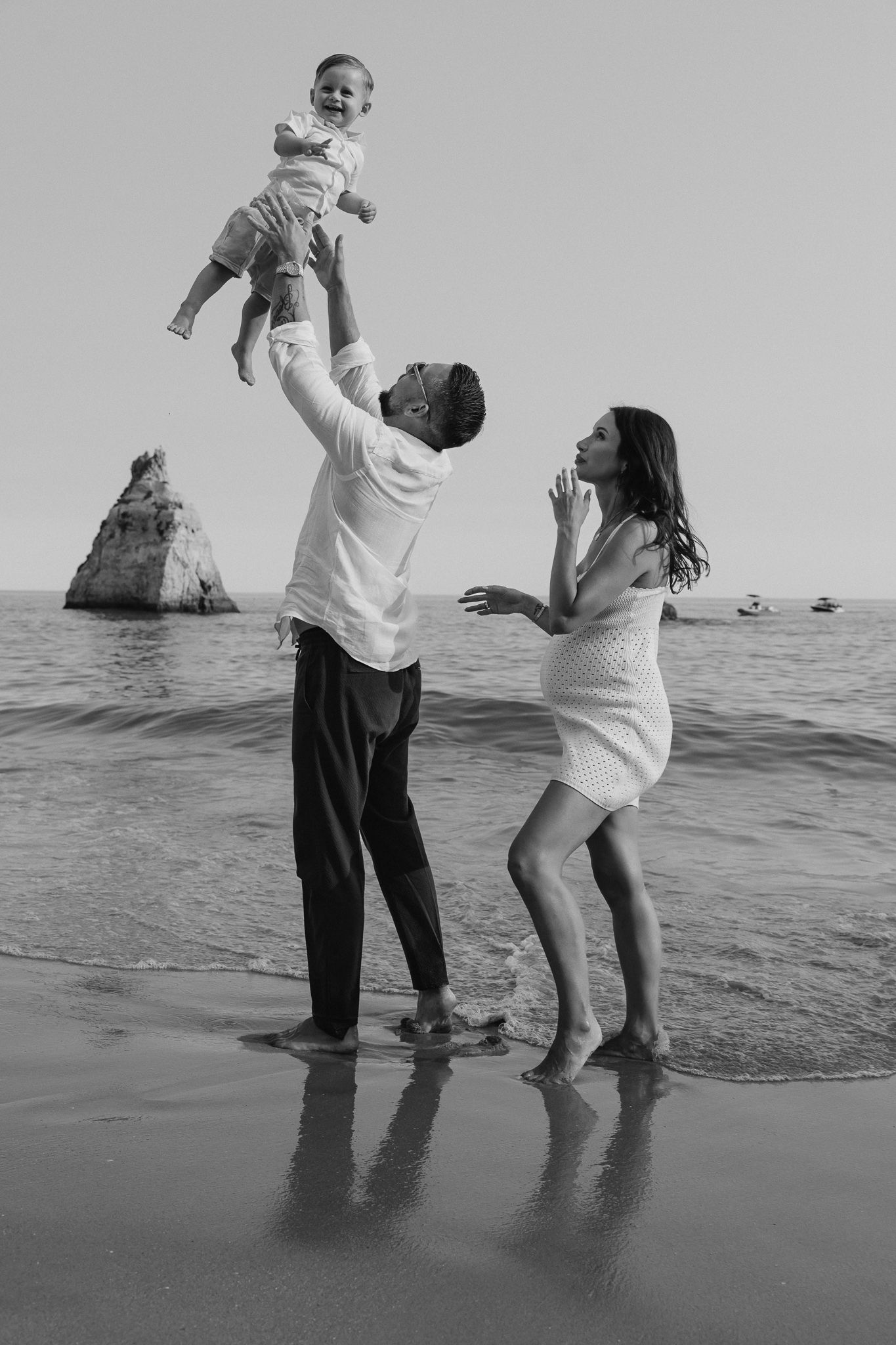 A playful beach scene with people splashing and dancing in the ocean waves in black and white.