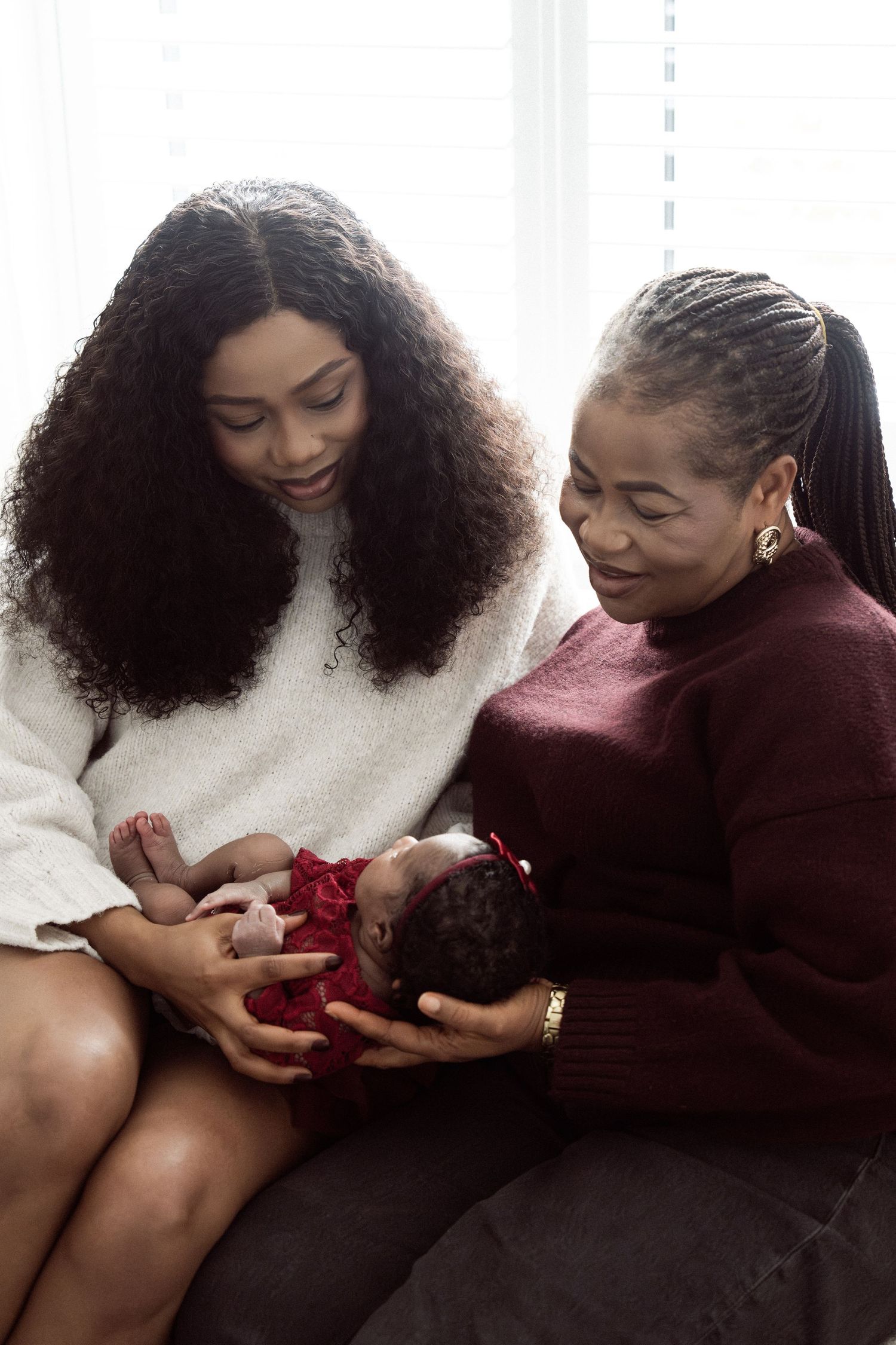 Two women admiring a newborn baby dressed in red, sharing a tender family moment together.