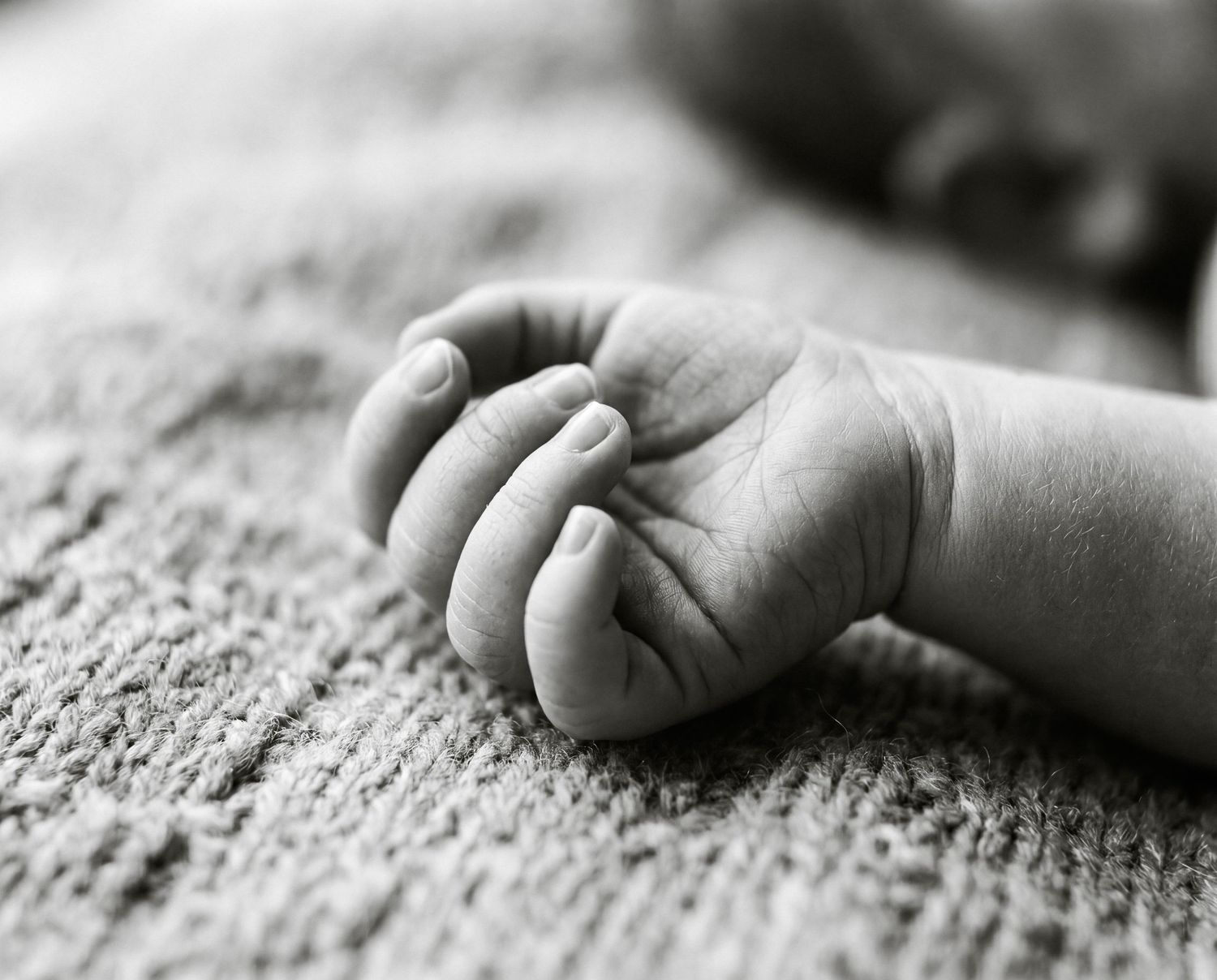 Black and white close-up photo of a newborn baby's tiny hand resting on a soft textured blanket.