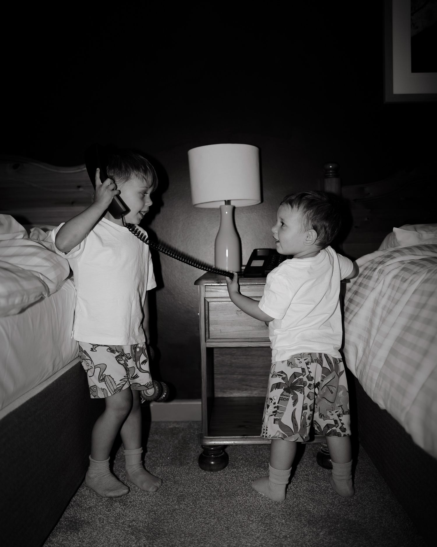 Two young children in matching shorts playing in a bedroom at night.