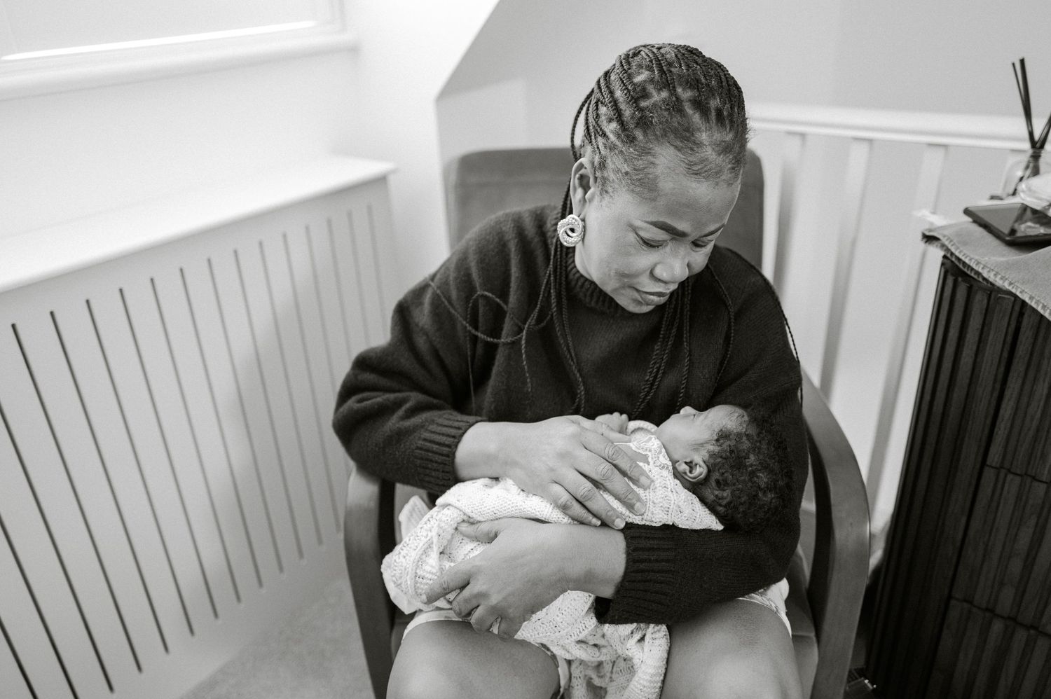 Mother sitting in a chair lovingly holding her newborn baby in a black and white photo.