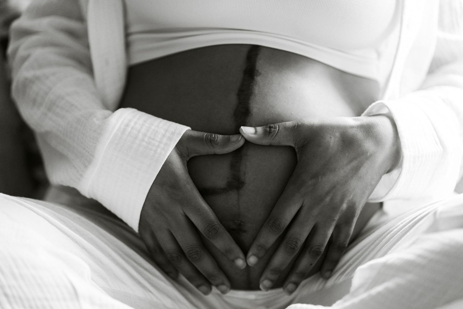 Black and white photo of pregnant woman forming heart shape on baby bump with her hands
