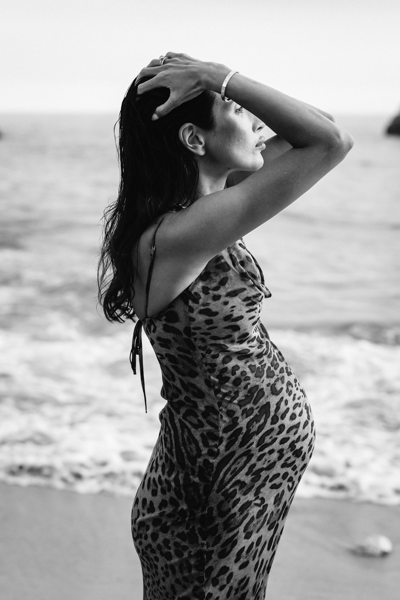Black and white photo of a woman in a leopard print dress posing on a beach.