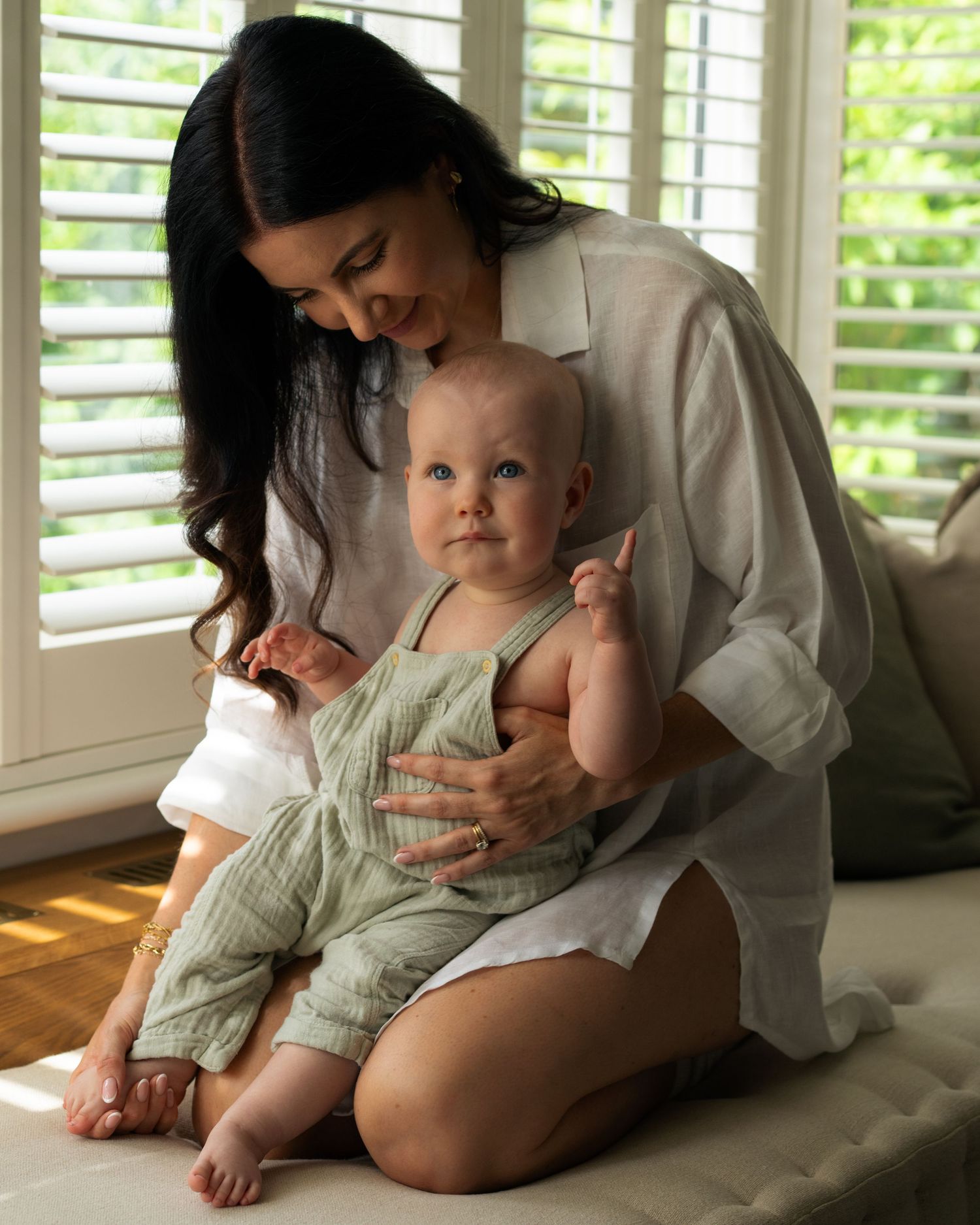 Sweet candid moments between caregiver and baby in sunlit room with plantation shutters.