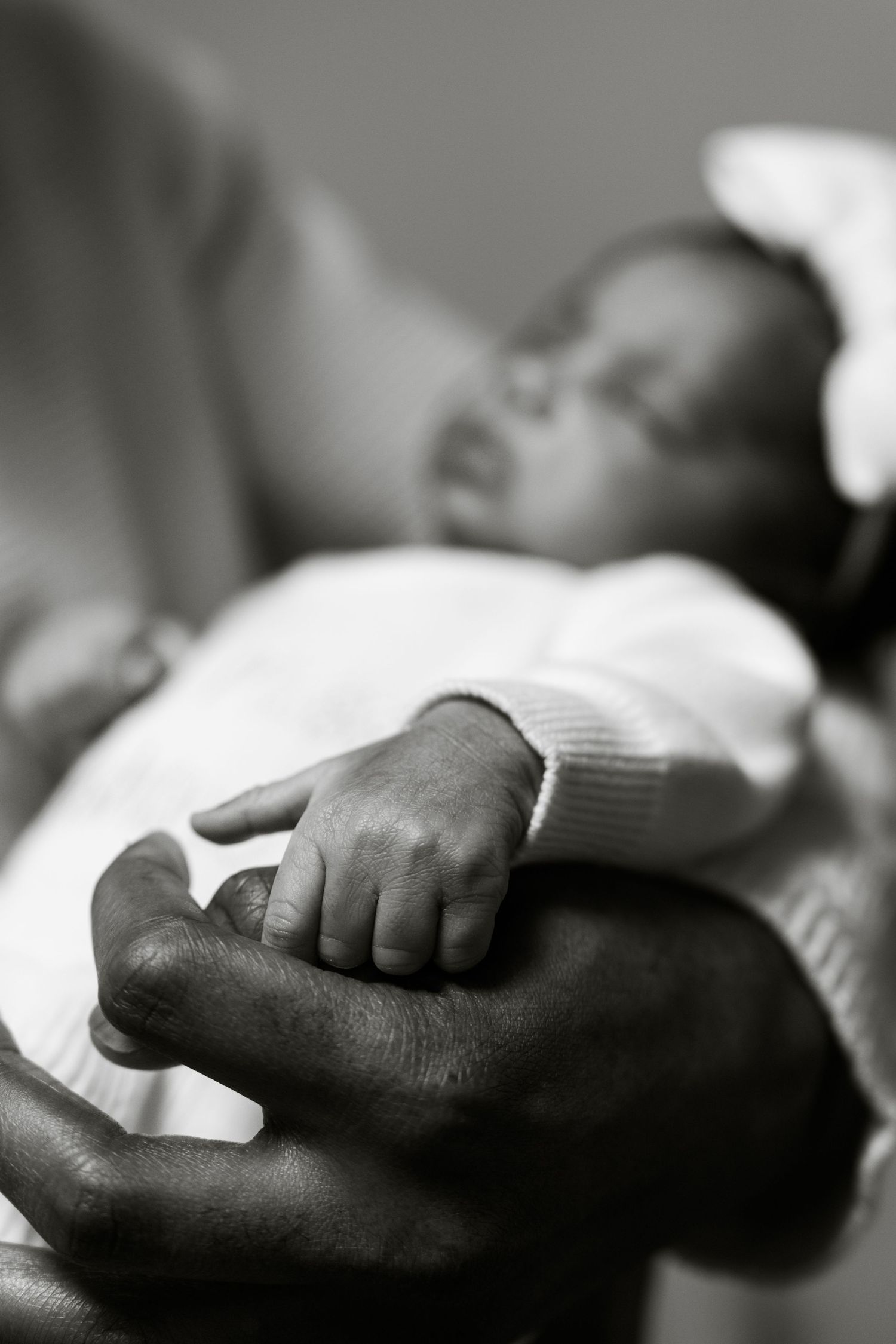 Black and white photo of a newborn baby grasping an adult finger while sleeping peacefully.