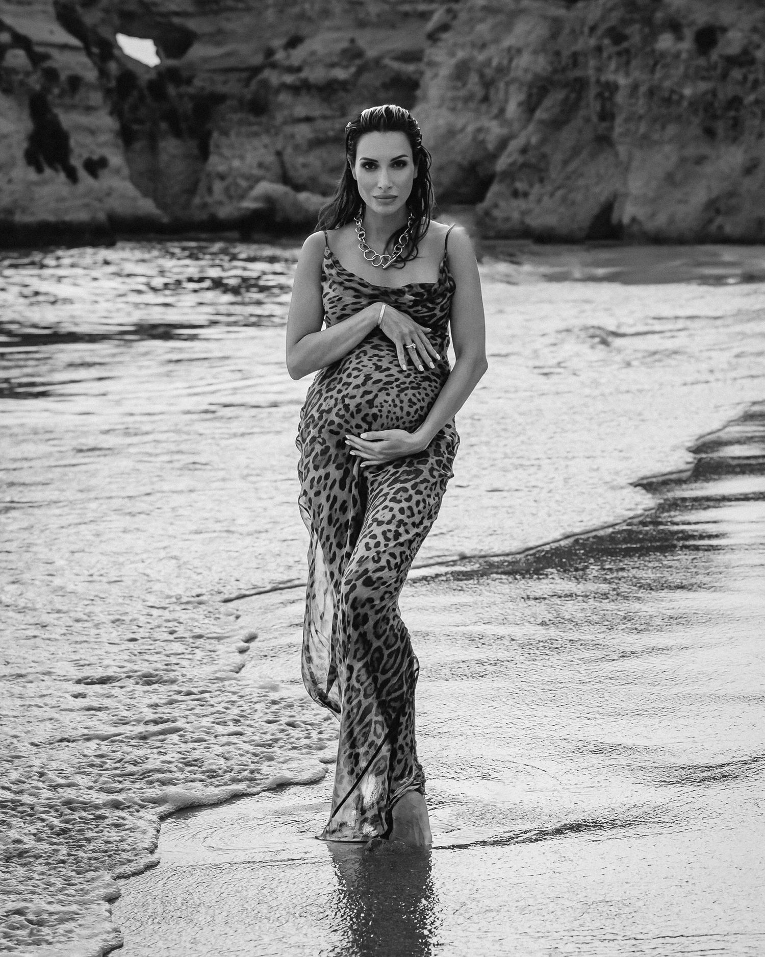 Woman in leopard print dress walking along beach shoreline in black and white photography.