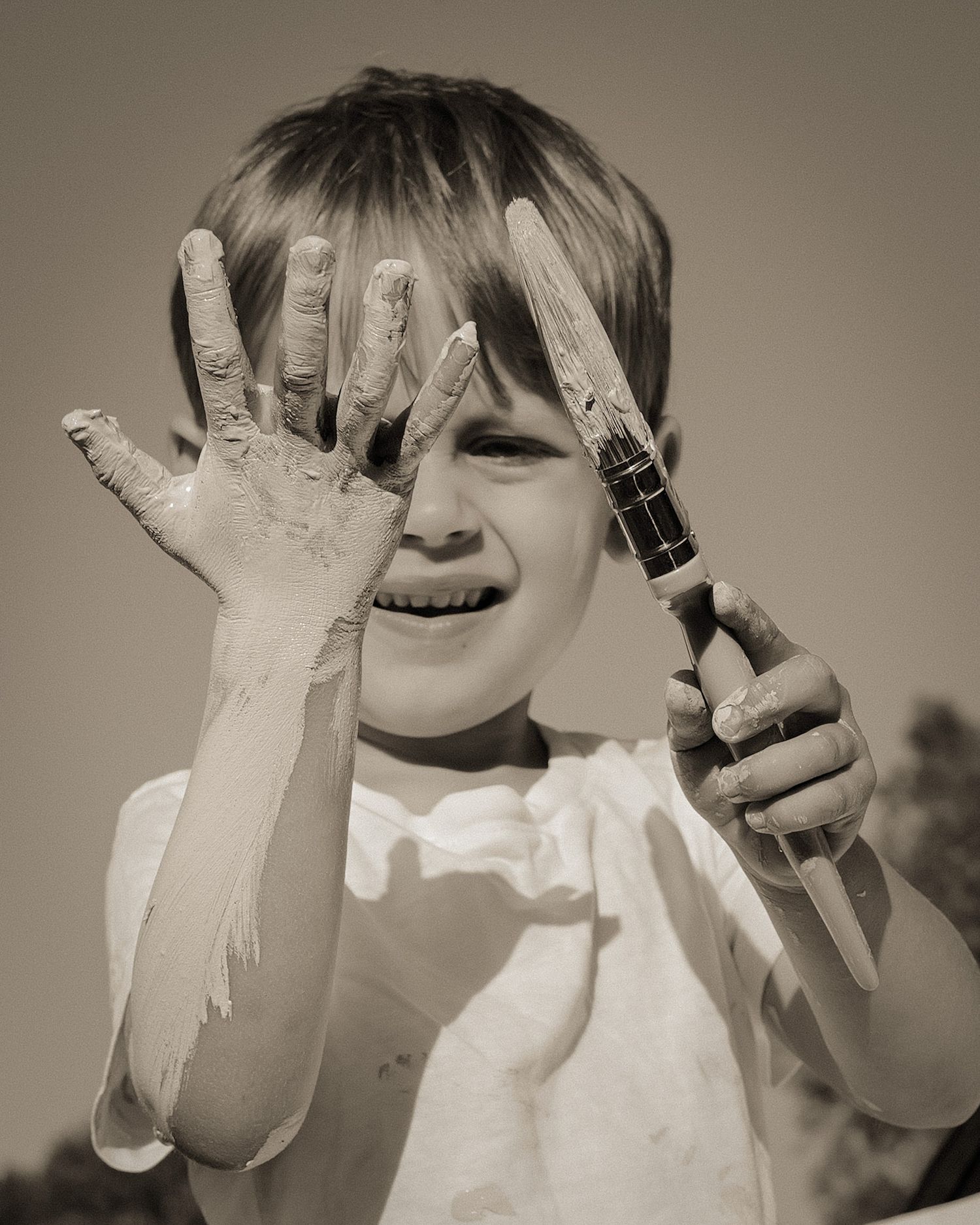 Young child showing messy painted hands and laughing with joy.