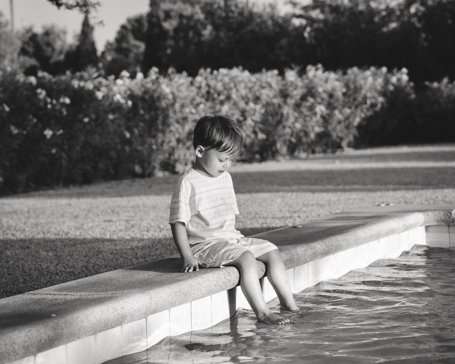 Black and white image of someone sitting at the edge of a swimming pool.