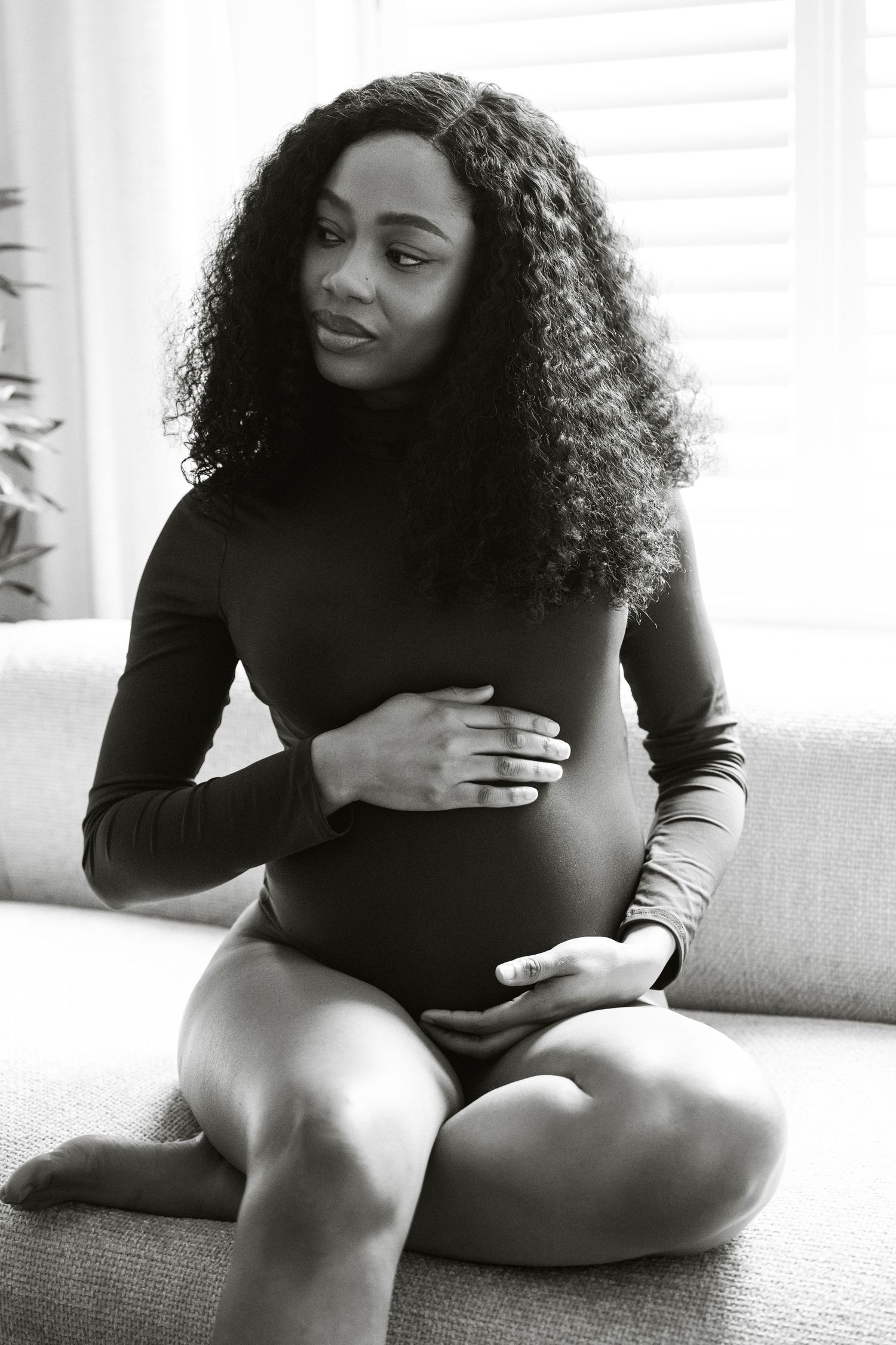 Black and white maternity portrait, expectant mother on sofa cradling baby bump | London maternity photographer by Inga Franlund