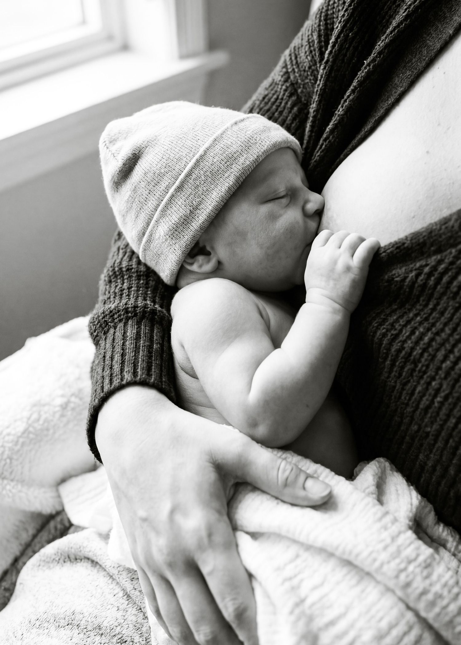 Black and white photo of a newborn baby in a knit hat breastfeeding, cradled in mother's arms.