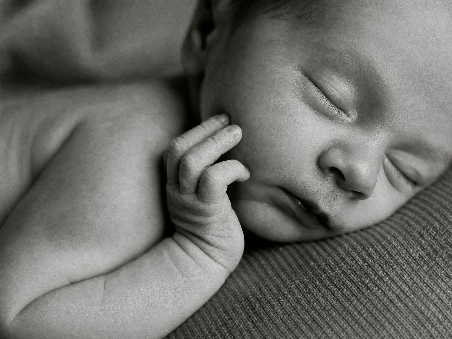 Black and white photo of a peaceful sleeping newborn baby with tiny fingers resting against cheek.