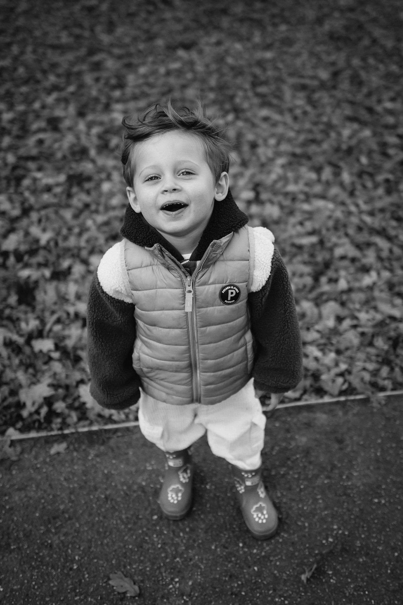 Black and white photos capture a child jumping and playing outdoors in a puffy vest.
