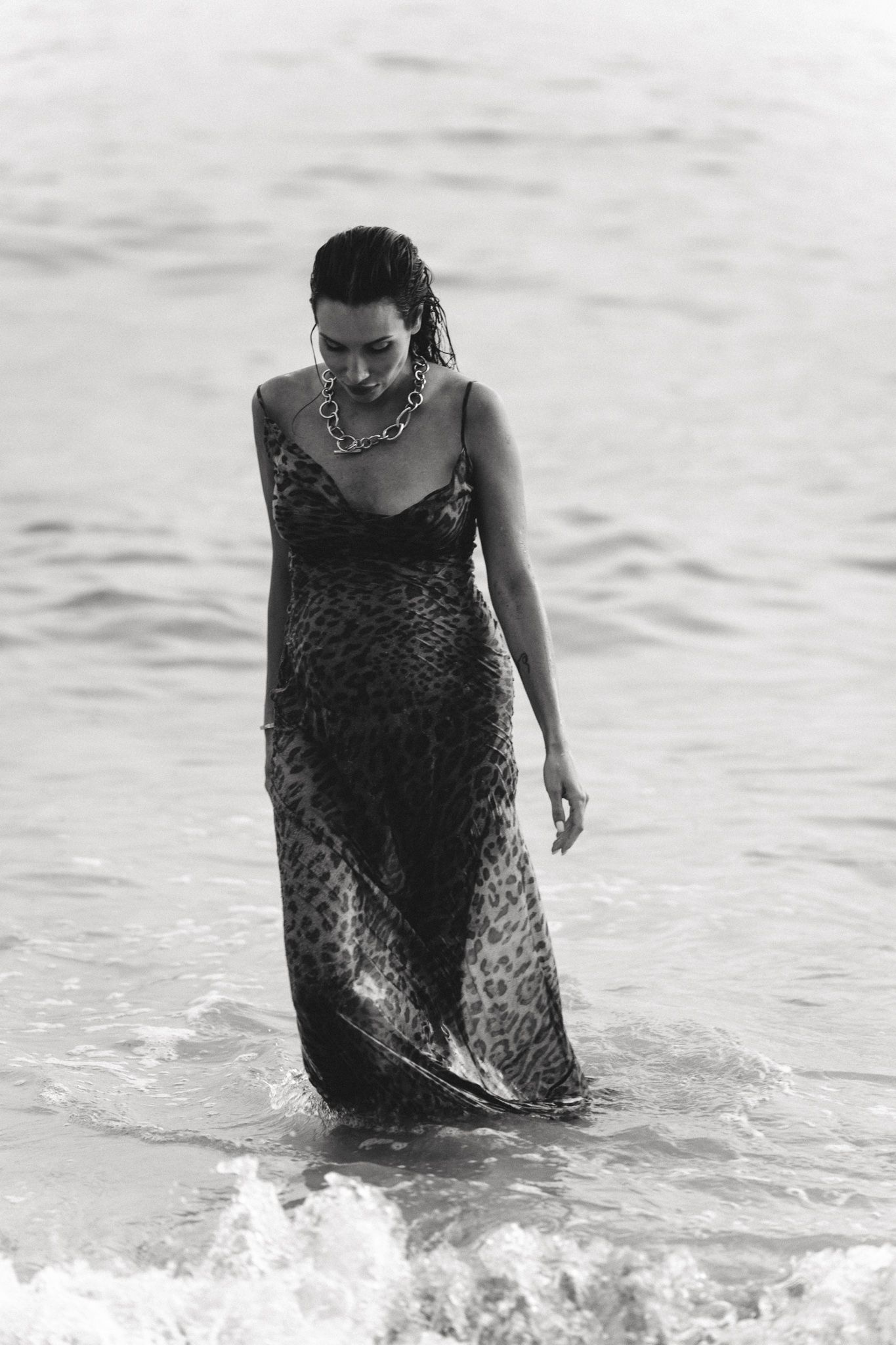 Woman wading through ocean waves in flowing leopard print dress.