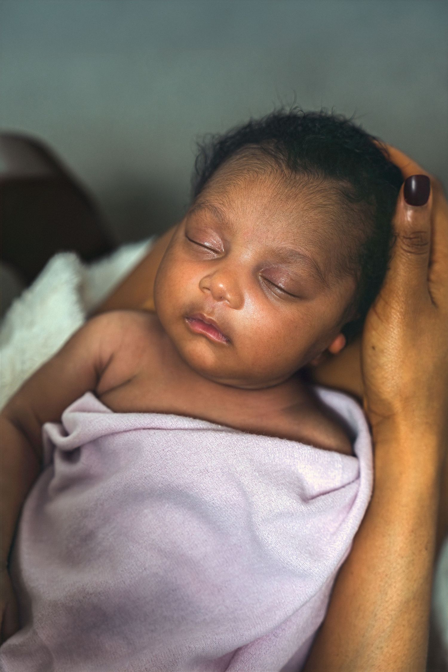 Peaceful newborn baby sleeping wrapped in a soft lavender blanket, cradled gently in caring hands.