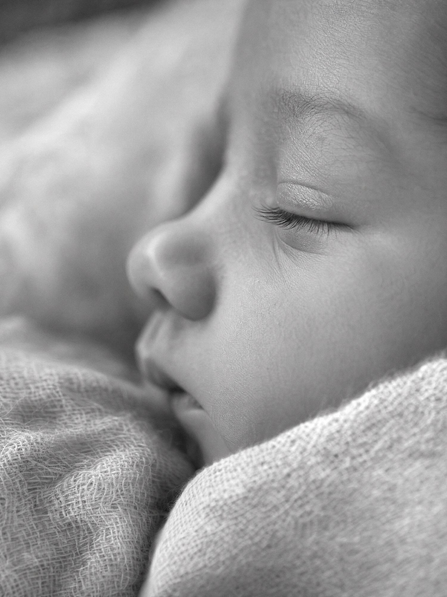 Black and white close-up photo of a peaceful sleeping newborn baby wrapped in a soft blanket.