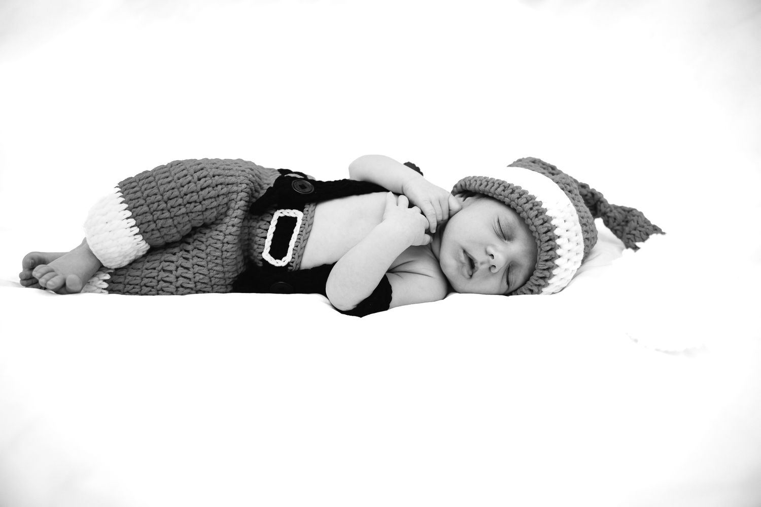 Sleeping baby wearing knit hat and outfit in black and white portrait.