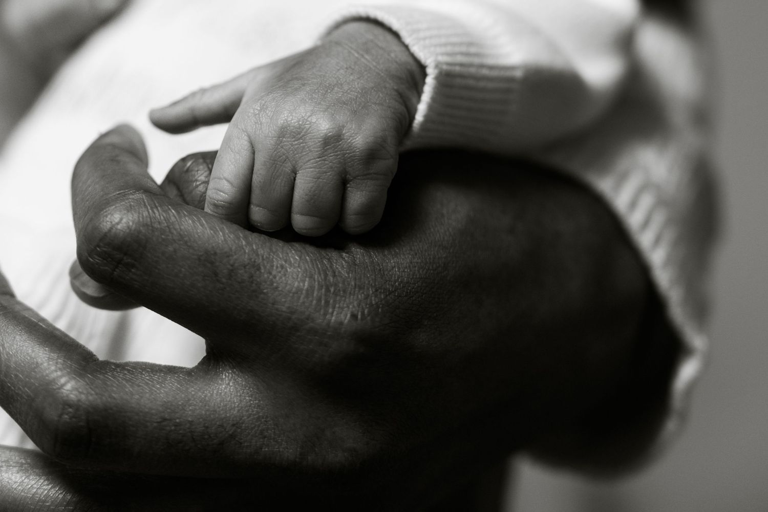 Black and white photo of a newborn baby's tiny hand gently gripping an adult's finger.