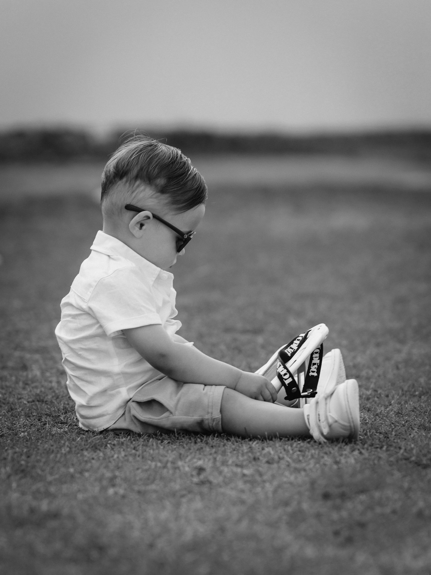 Black and white photo showing small feet in white shoes sitting on grass.