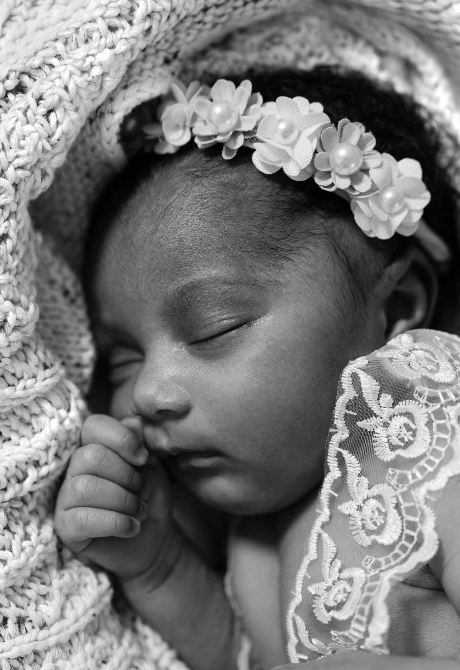 Close-up black and white portrait of a peaceful sleeping newborn baby girl wearing a delicate flower crown and lace dress.