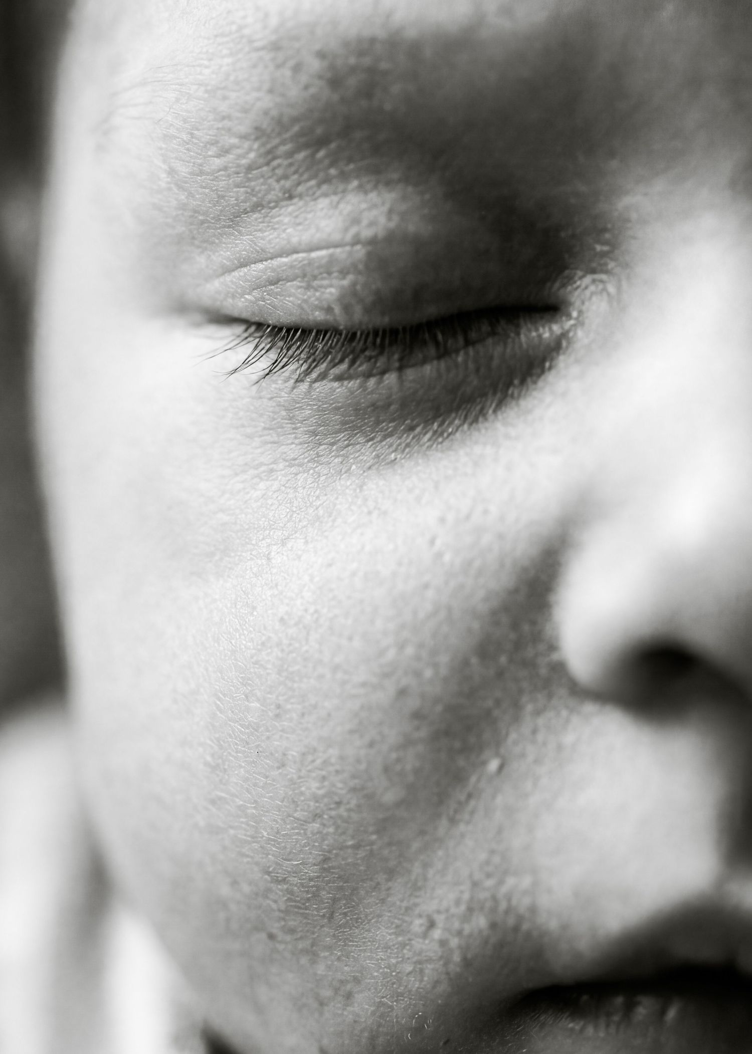 Close-up black and white photo of a sleeping newborn baby's face showing delicate eyelashes and soft skin.