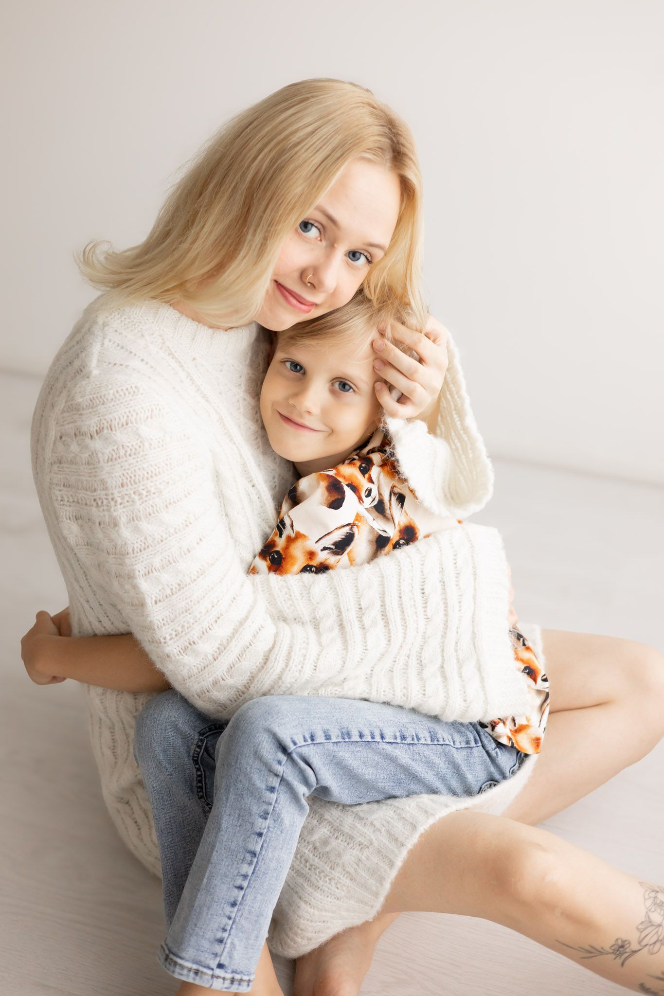 Person in white sweater and blue jeans poses against white background in artistic portrait series.
