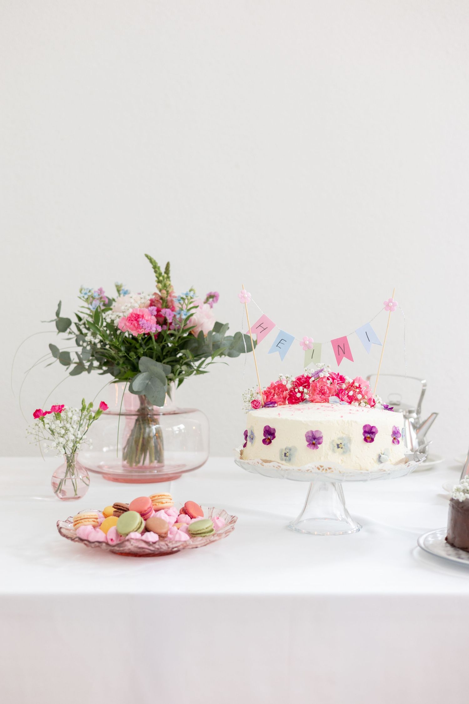 Ristiäisten tarjoilupöytä pinkein koristein. Kaunis kukkakimppu, kakku ja macaron-leivoksia.