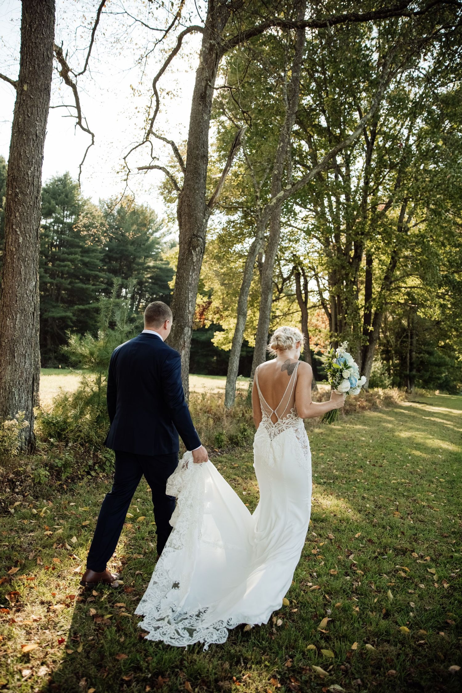 Newlyweds walking through a wooded area with autumn trees in the background.