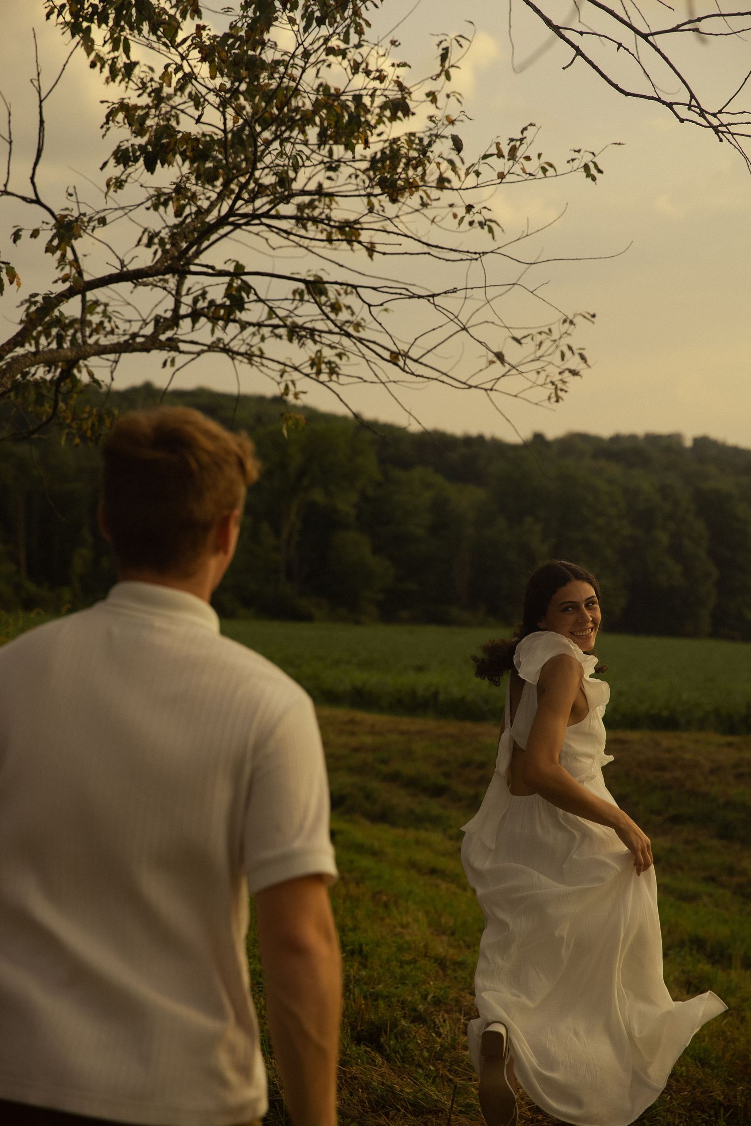 A couple in white clothing embracing in a golden sunset field.