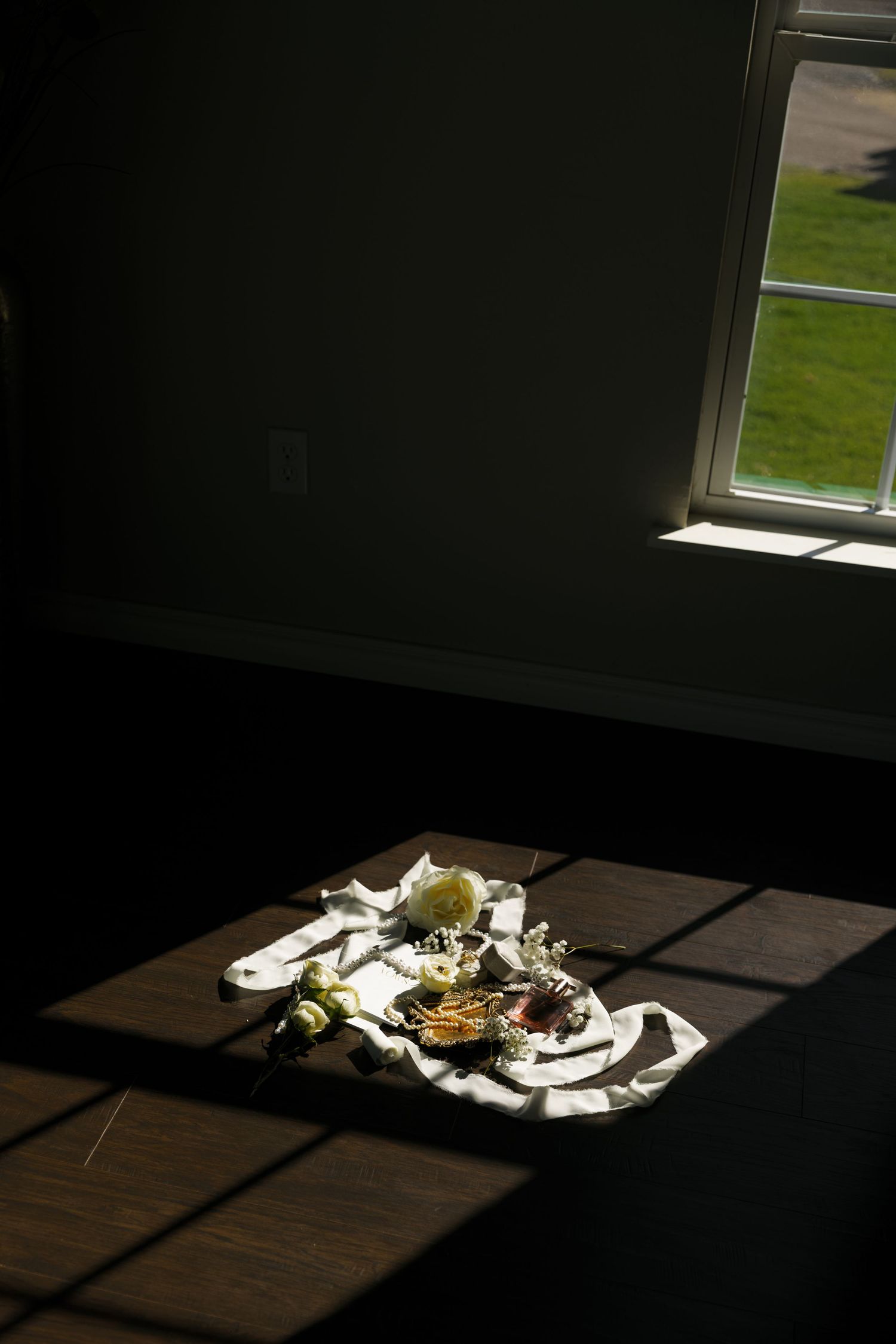 Sunlight casts dramatic shadows on a wooden floor, illuminating scattered white objects in a dark room.