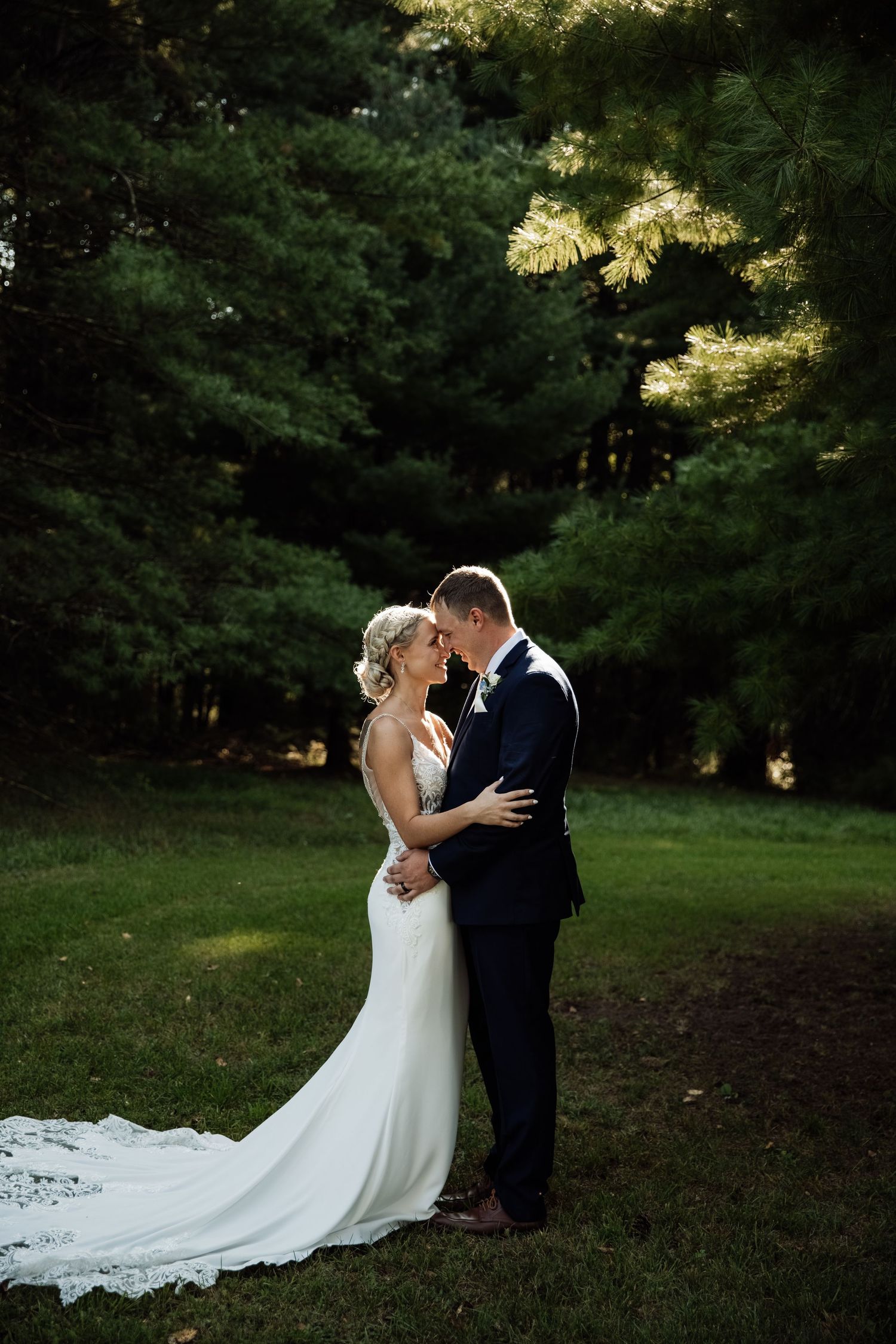 Elegant wedding couple shares tender moments on a grassy lawn surrounded by trees.
