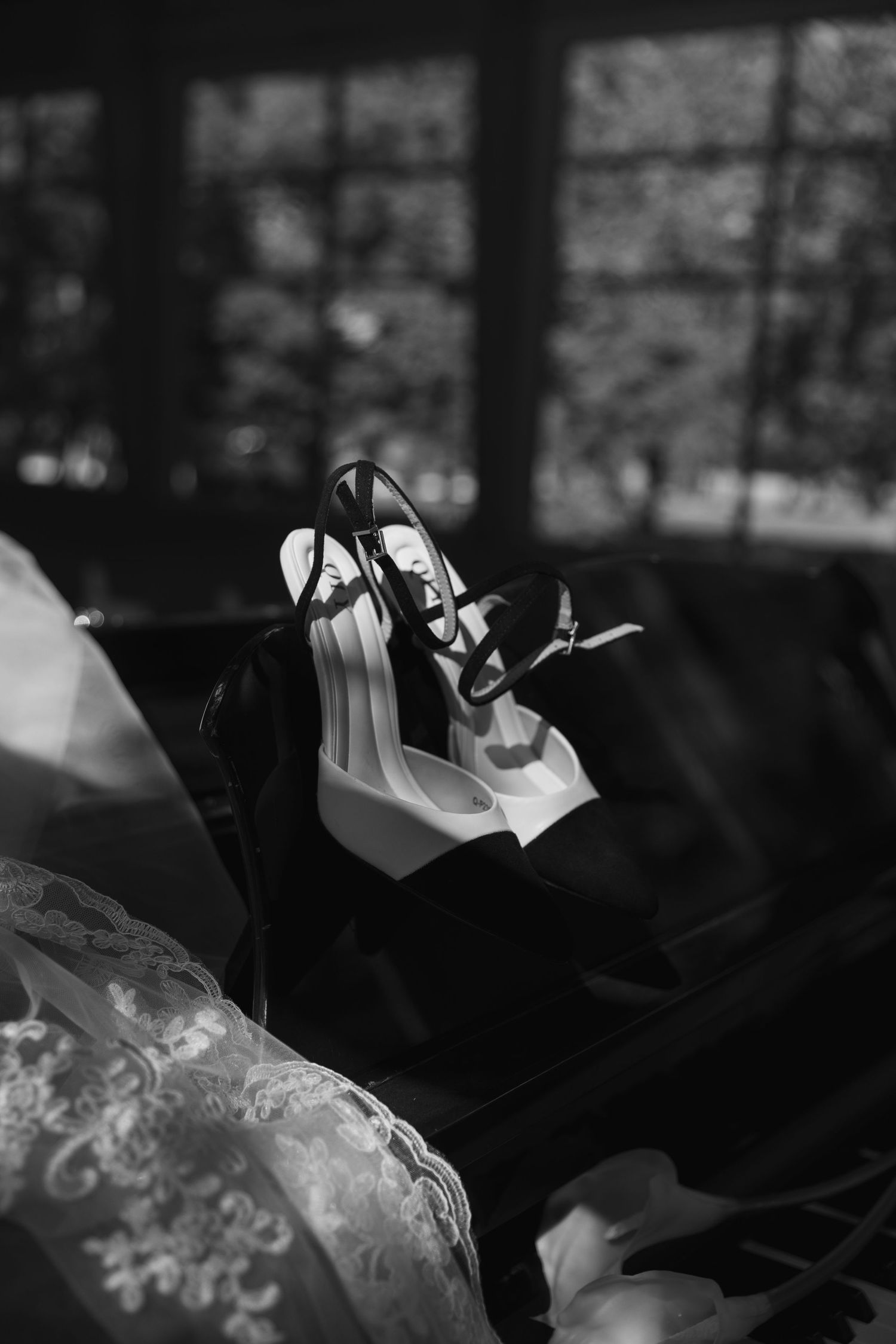 Black and white photo of elegant high heeled shoes resting on dark fabric with window light in background.