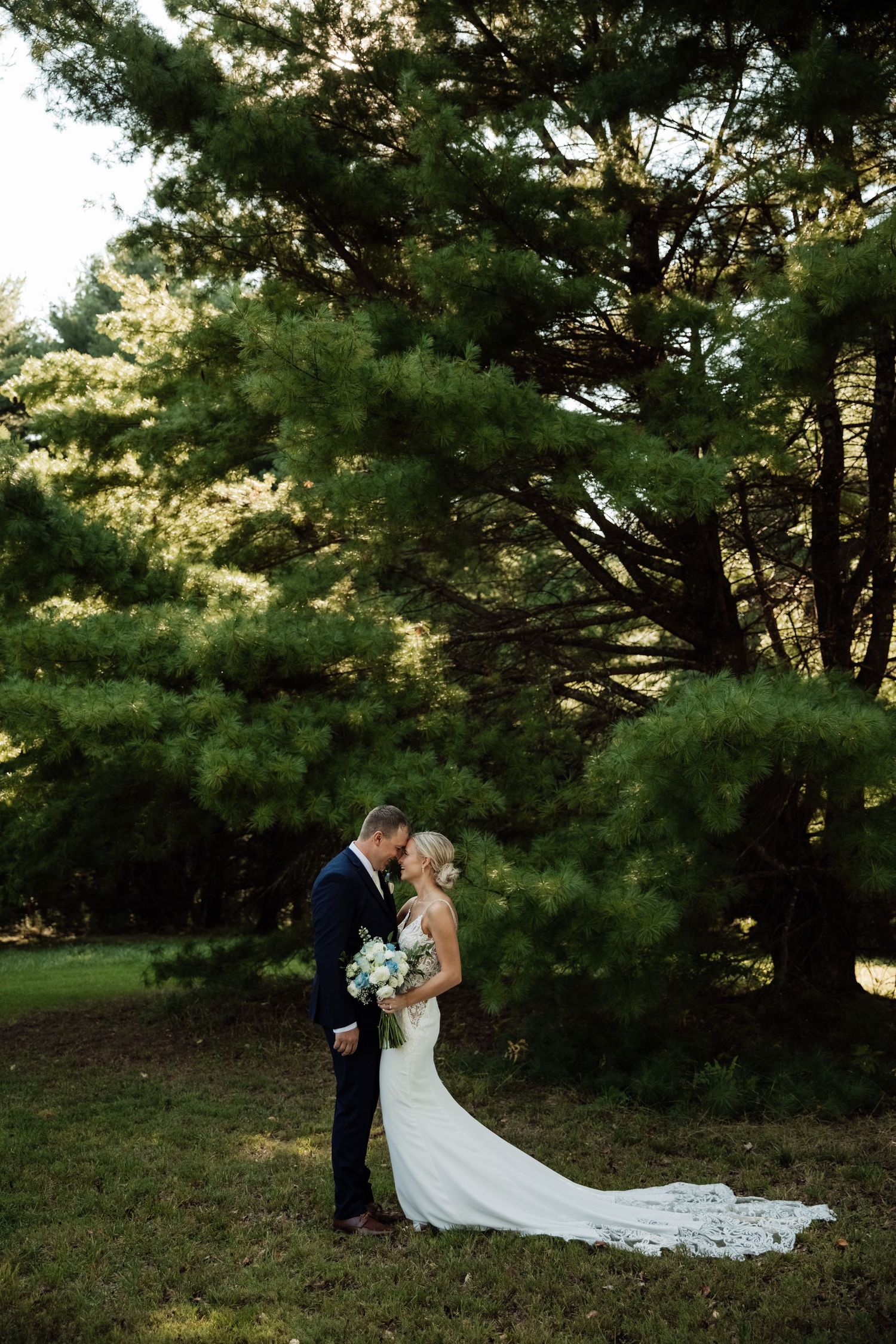 Wedding couple embracing in a scenic garden setting with pine trees.
