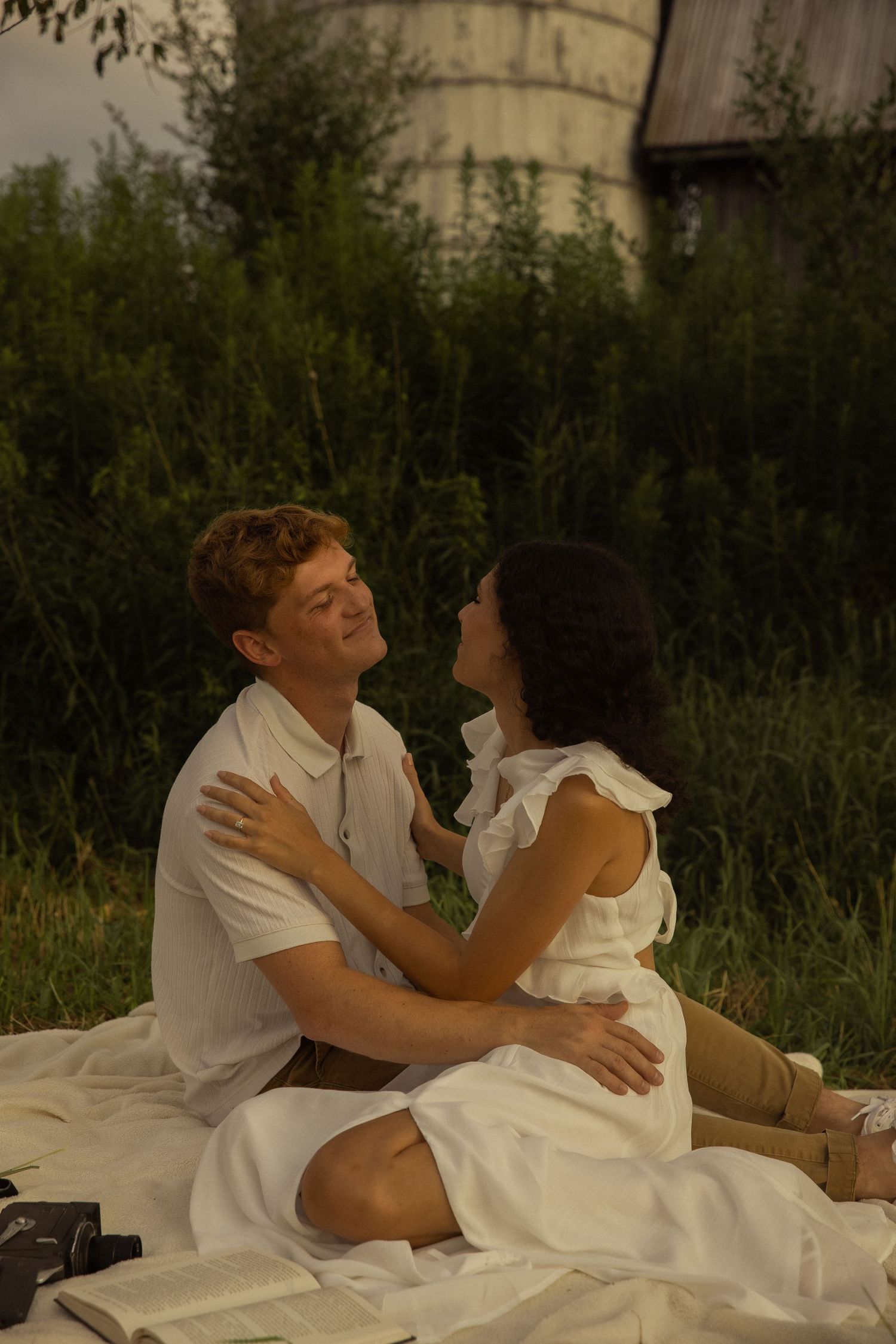 A romantic couple in white clothing lying together on a blanket outdoors.