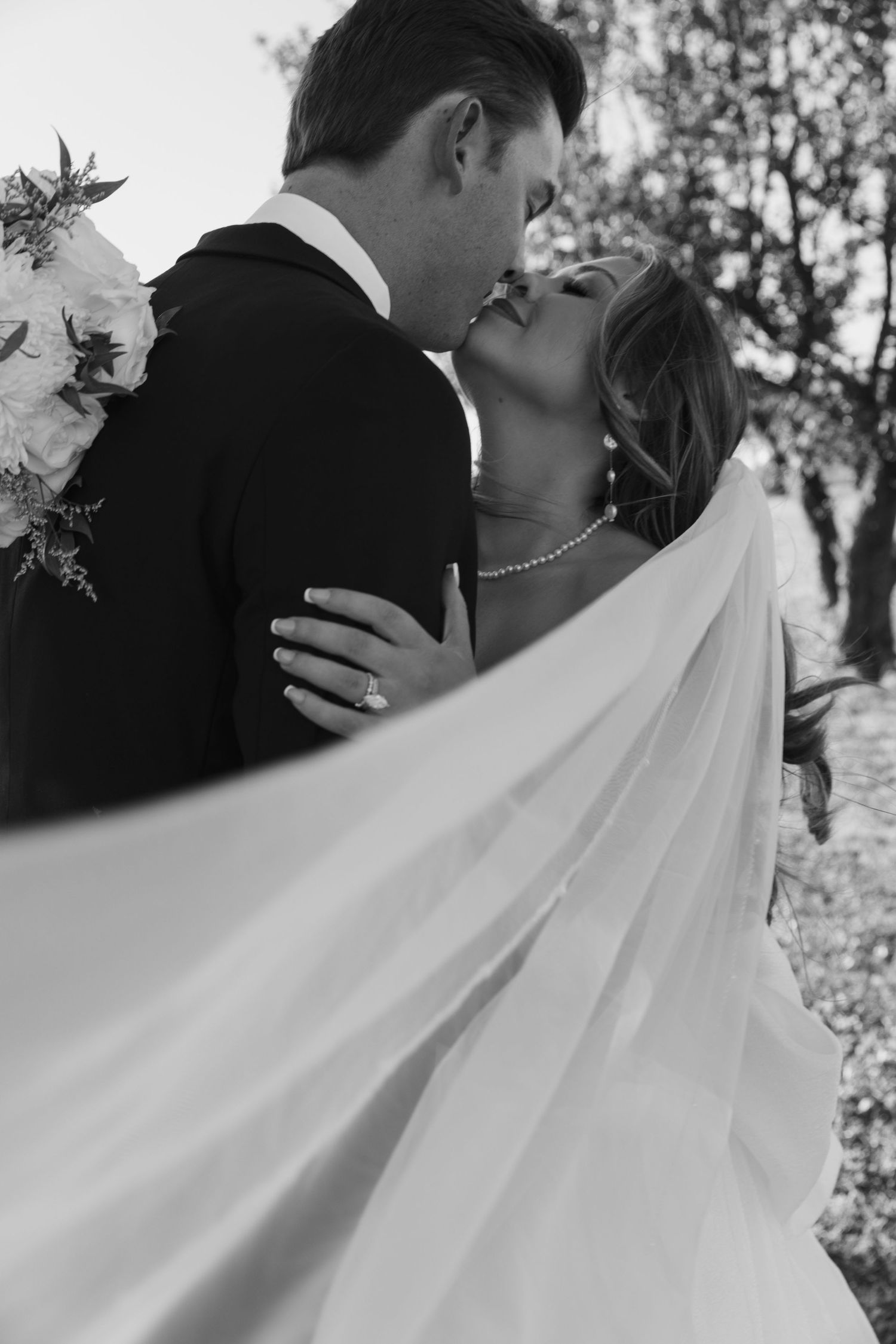A romantic black and white wedding photo series showing close-up shots of a couple kissing with flowing white veil details.