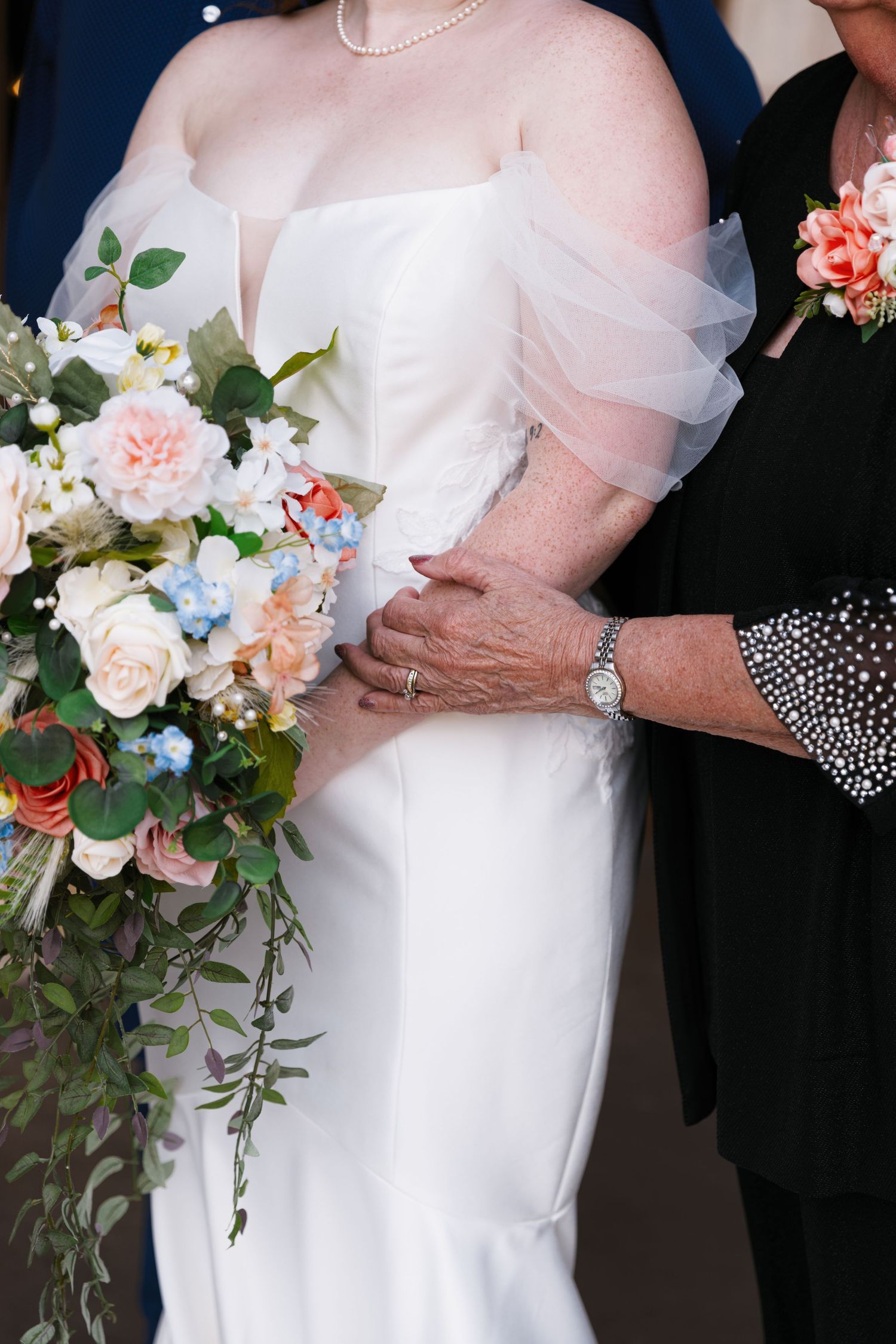 A bridal bouquet featuring pink and white flowers with cascading greenery against a white wedding dress.