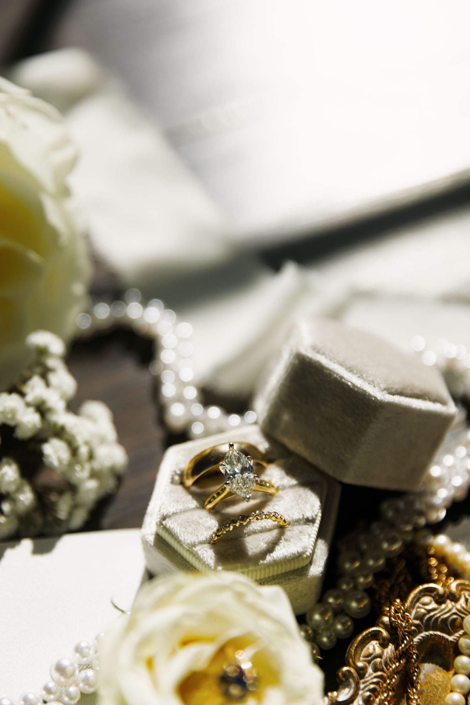 Elegant wedding rings nestled among delicate white flowers and golden jewelry details on a dark surface.