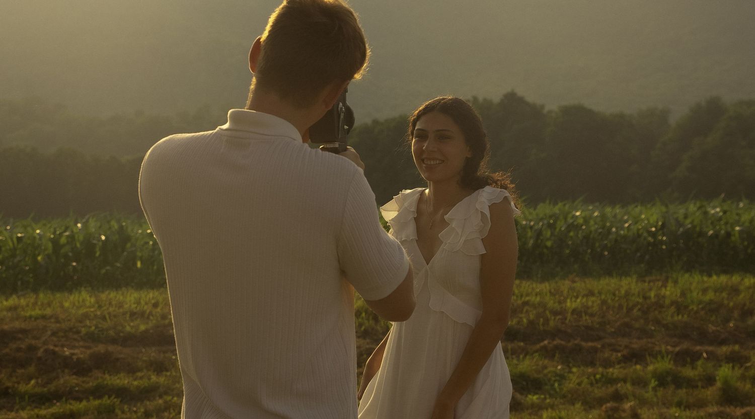 Silhouettes of two people standing in a field at sunset with mountains in the background.