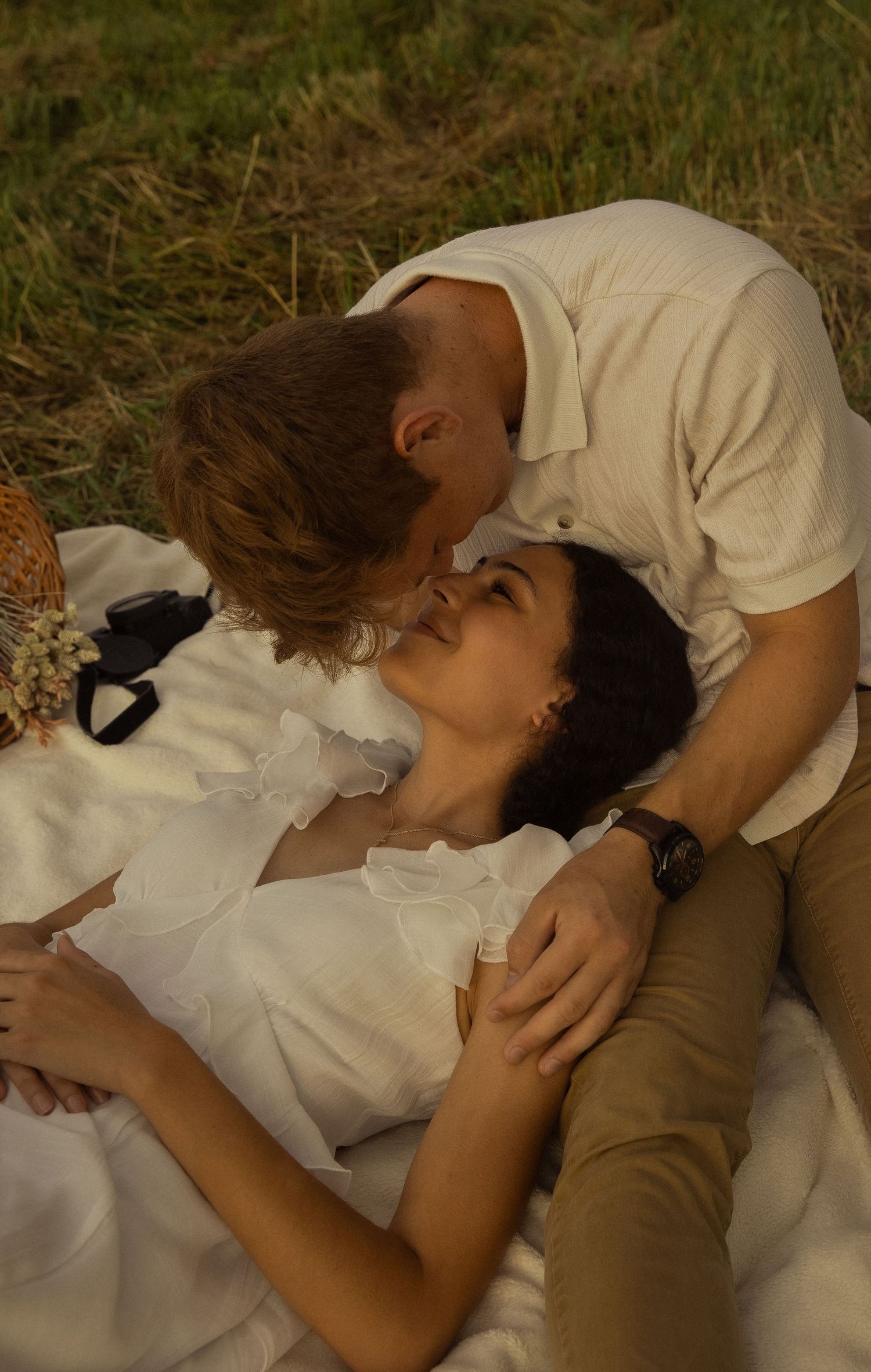 Two people in white clothing resting intimately on a blanket in nature.