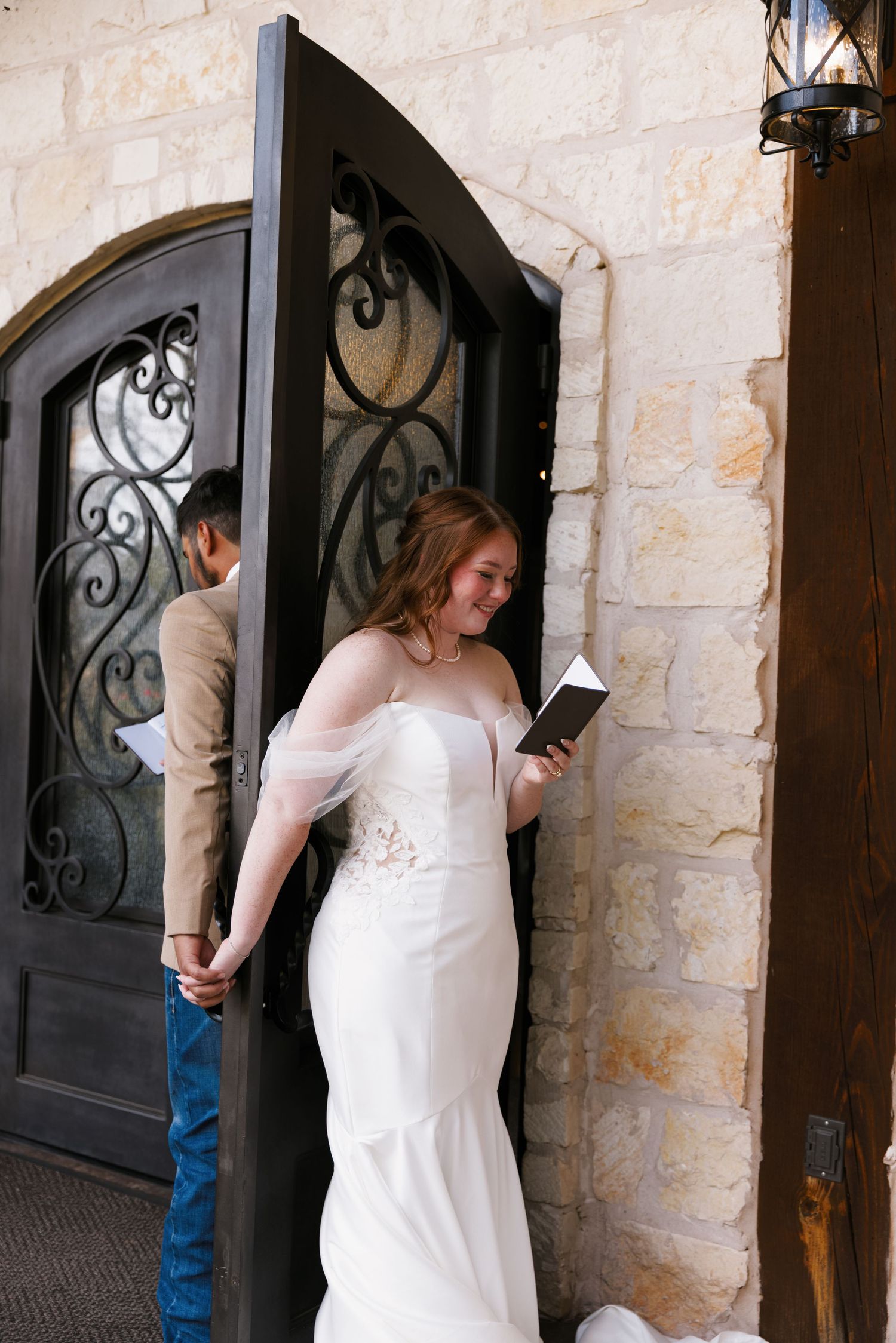 A person in a white dress opens a decorative iron door against a stone wall.