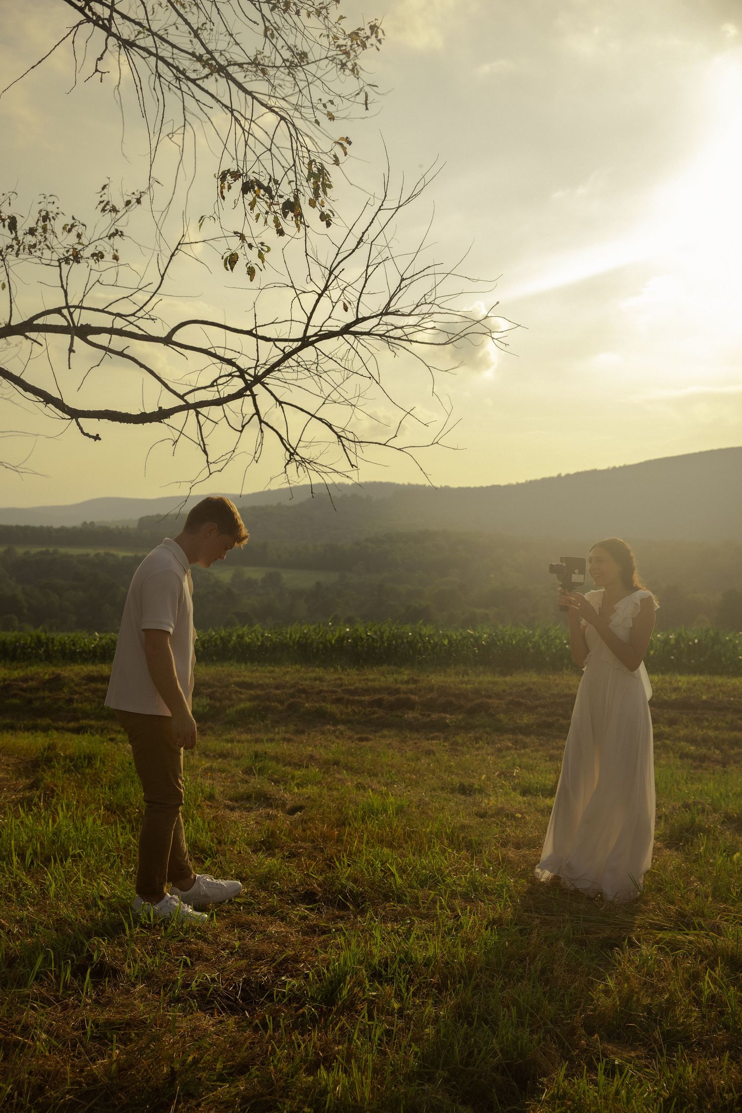 Couple in white and brown clothing walking in a field during golden hour.