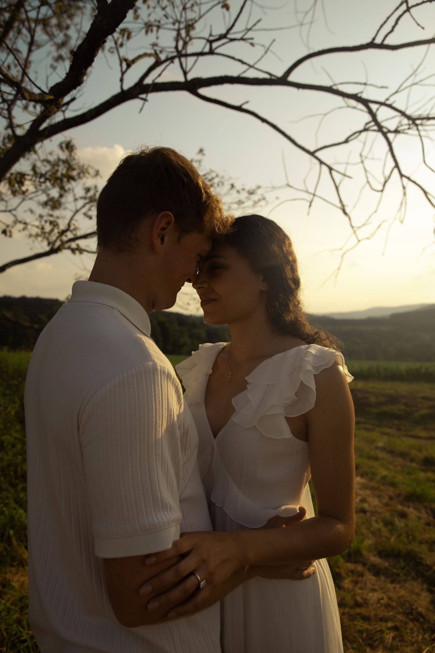 Couple in white clothing sharing an intimate moment at sunset in a field.