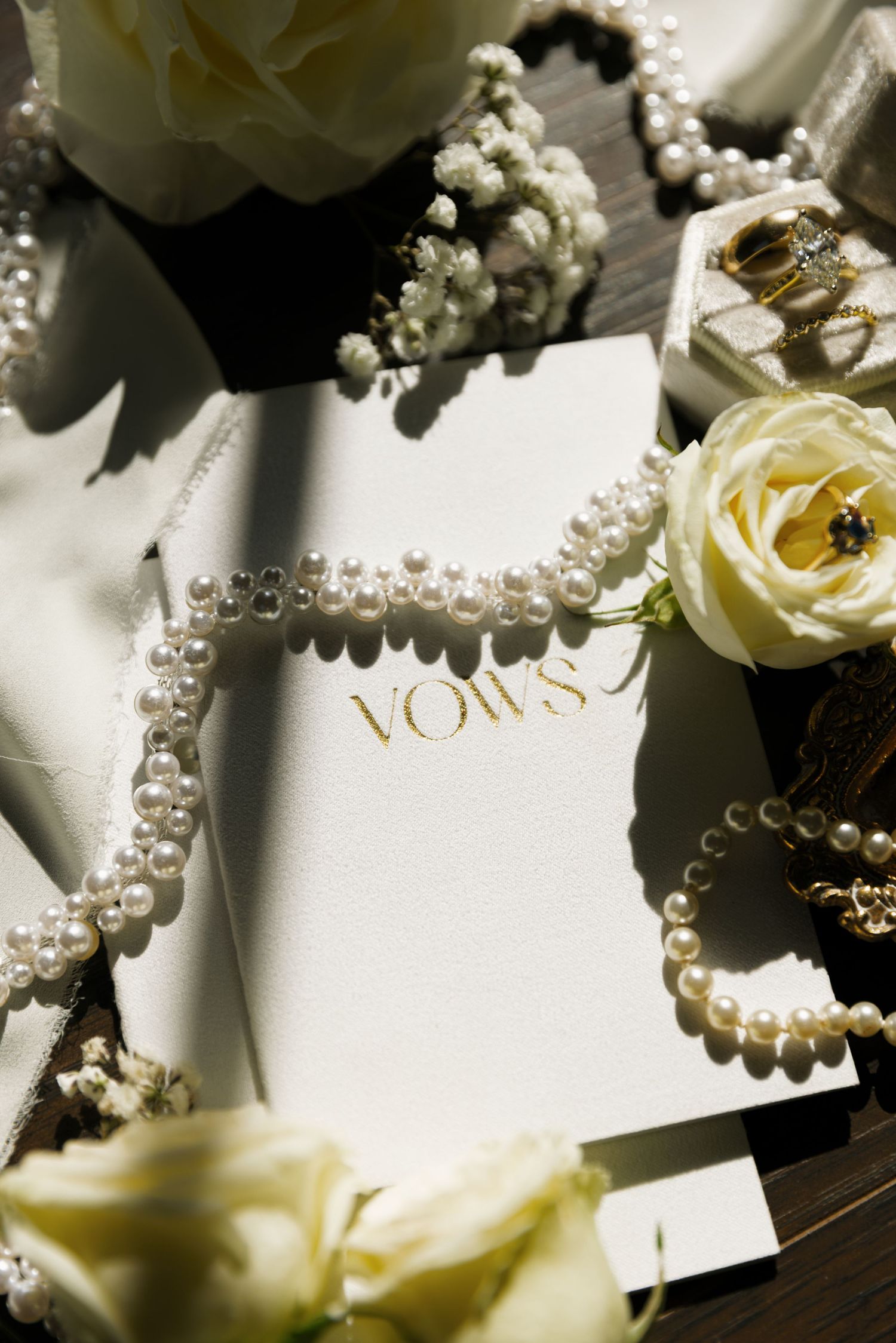 Wedding vows card surrounded by delicate white roses and a string of elegant pearls in natural light.