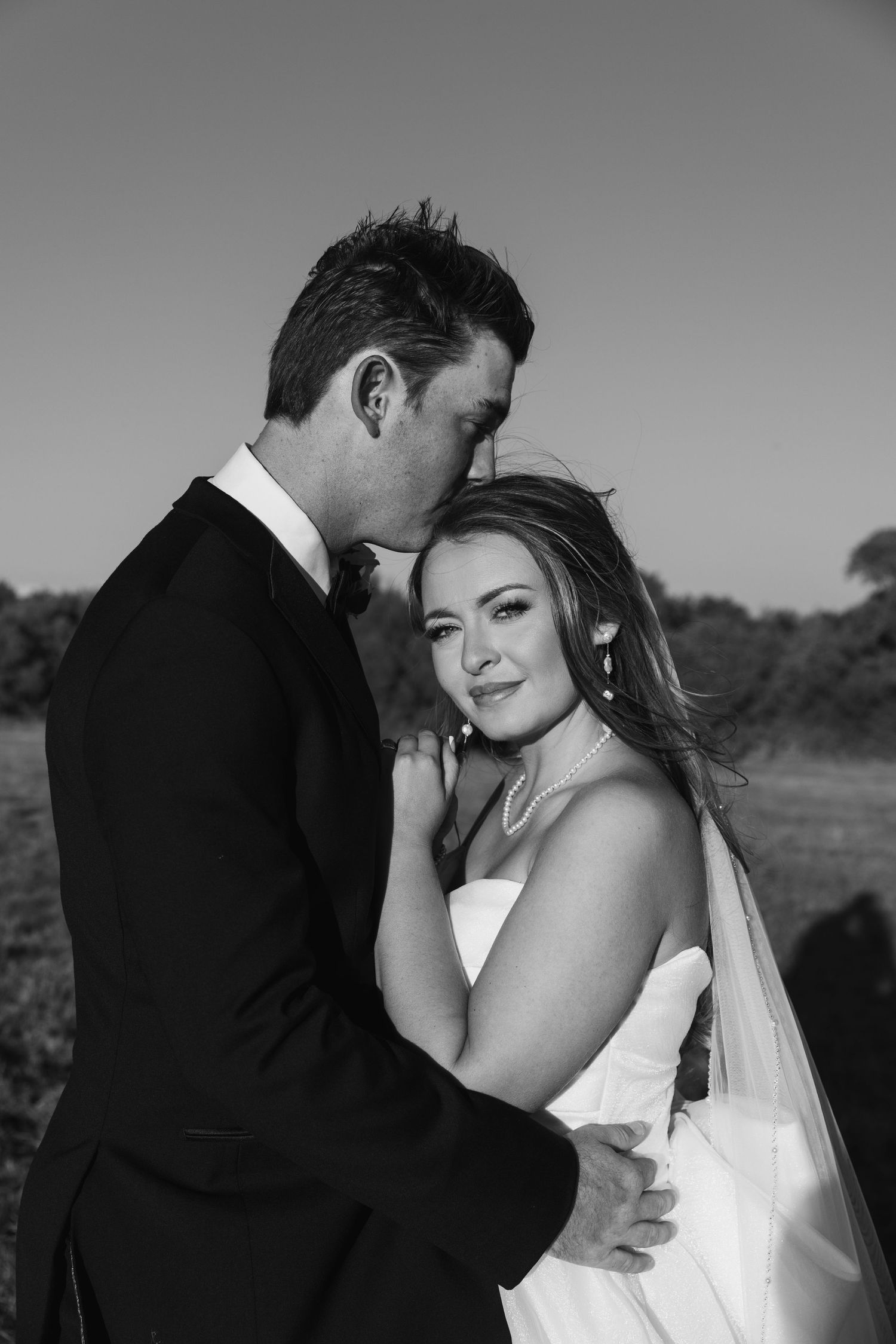A romantic black and white wedding photo series showing intimate moments between newlyweds embracing outdoors.