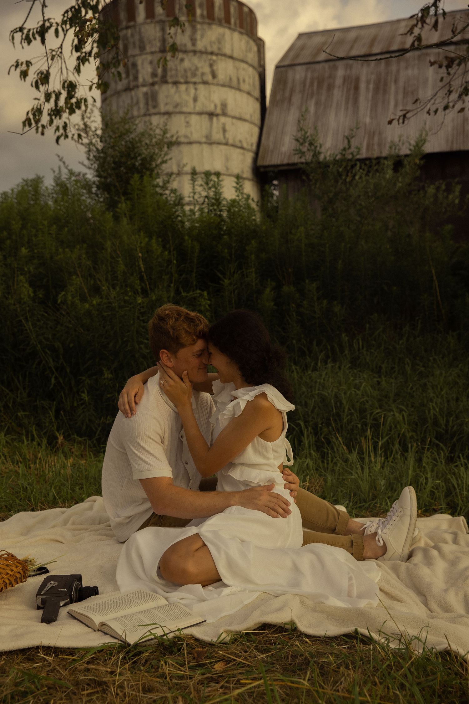 A couple relaxing on a blanket near industrial silos at dusk.