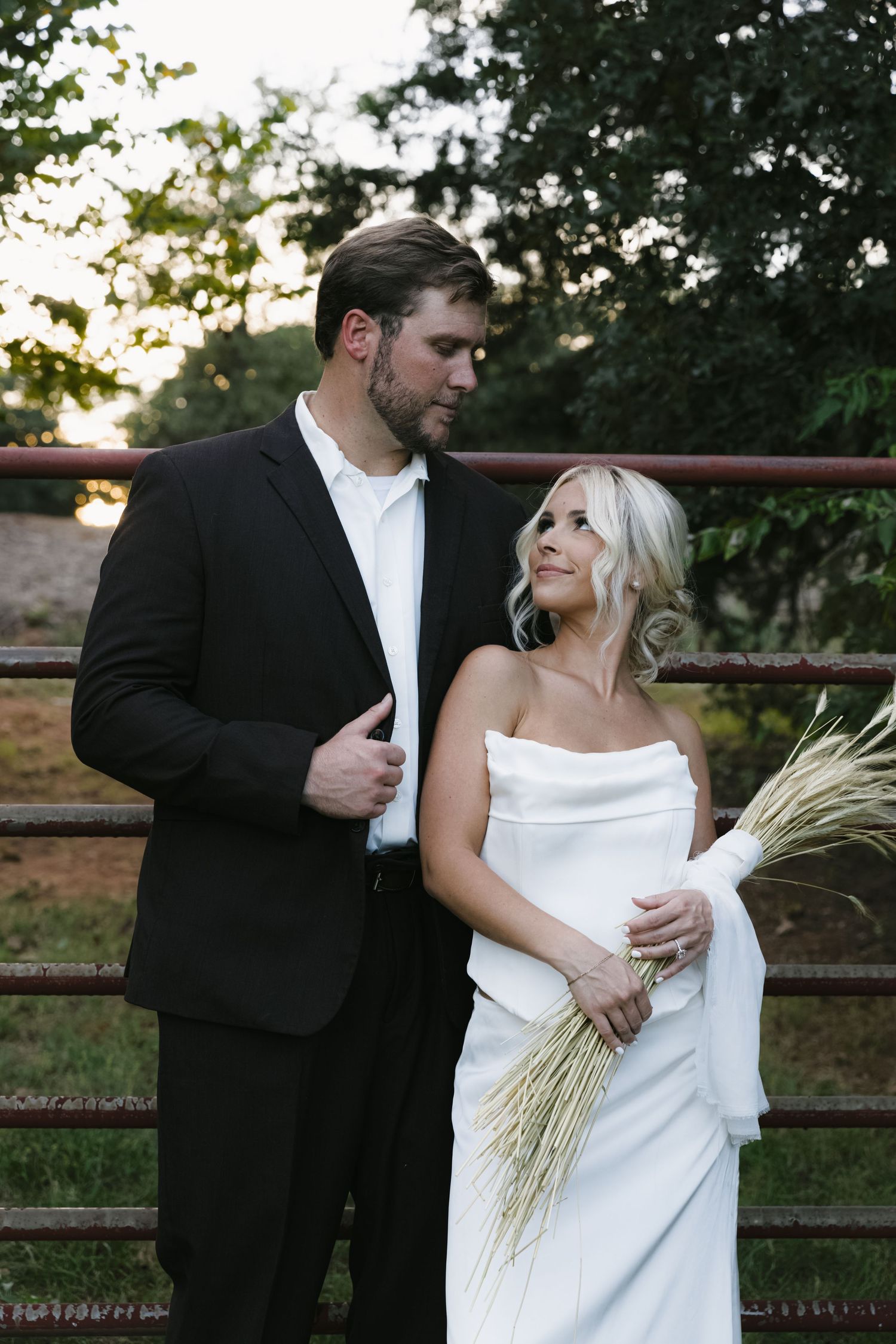 Romantic outdoor wedding portraits with couple against rustic fence at sunset.