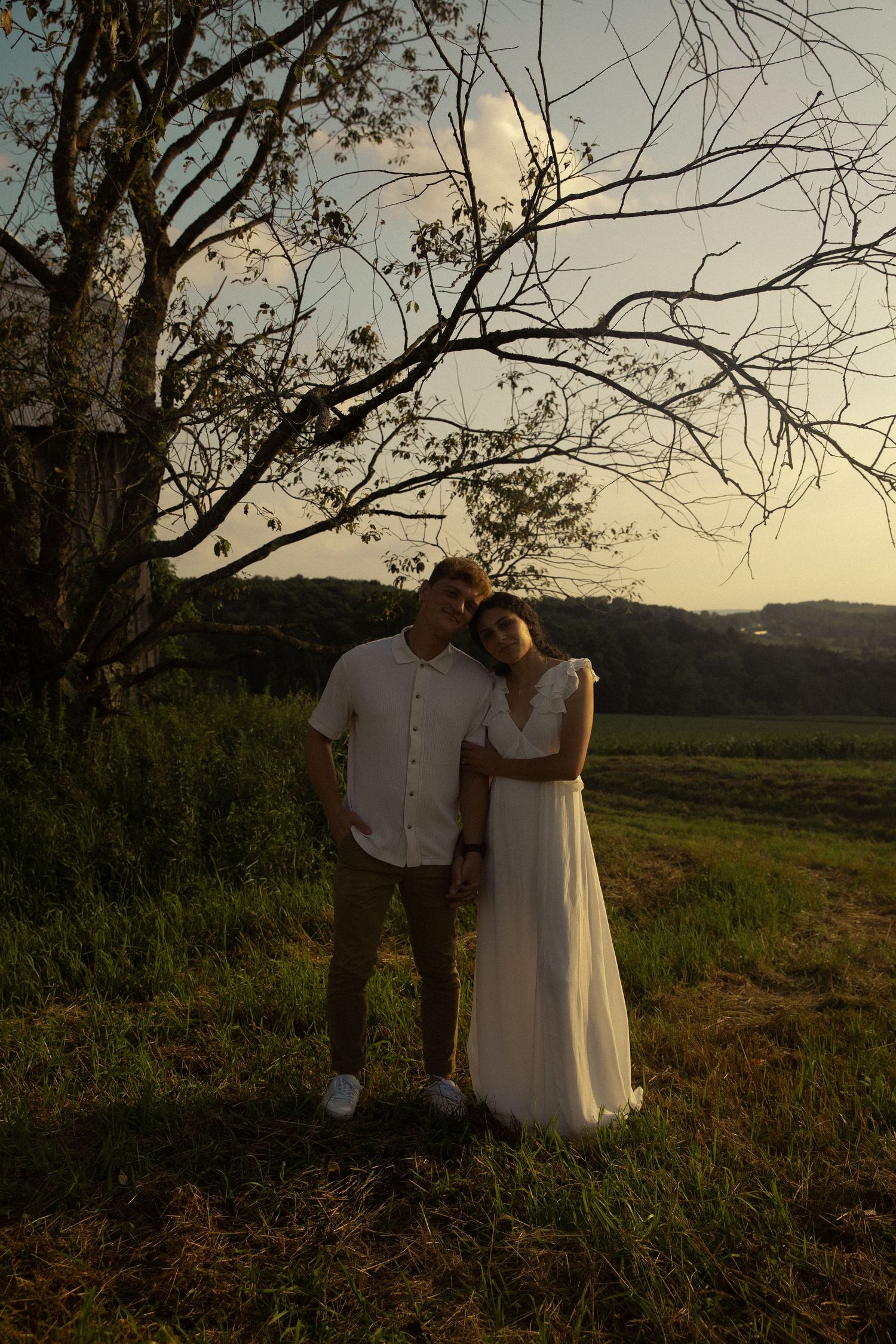 Two people in white clothing standing together in a field during sunset.