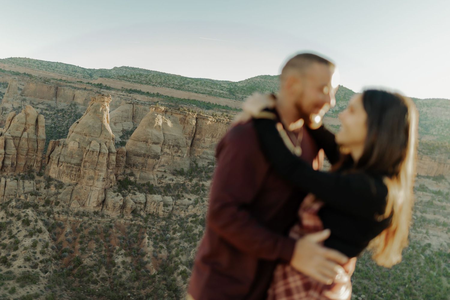 enagagement photoshoot with mountains in background couple smiling and holding each other  close in Colorado National Monument