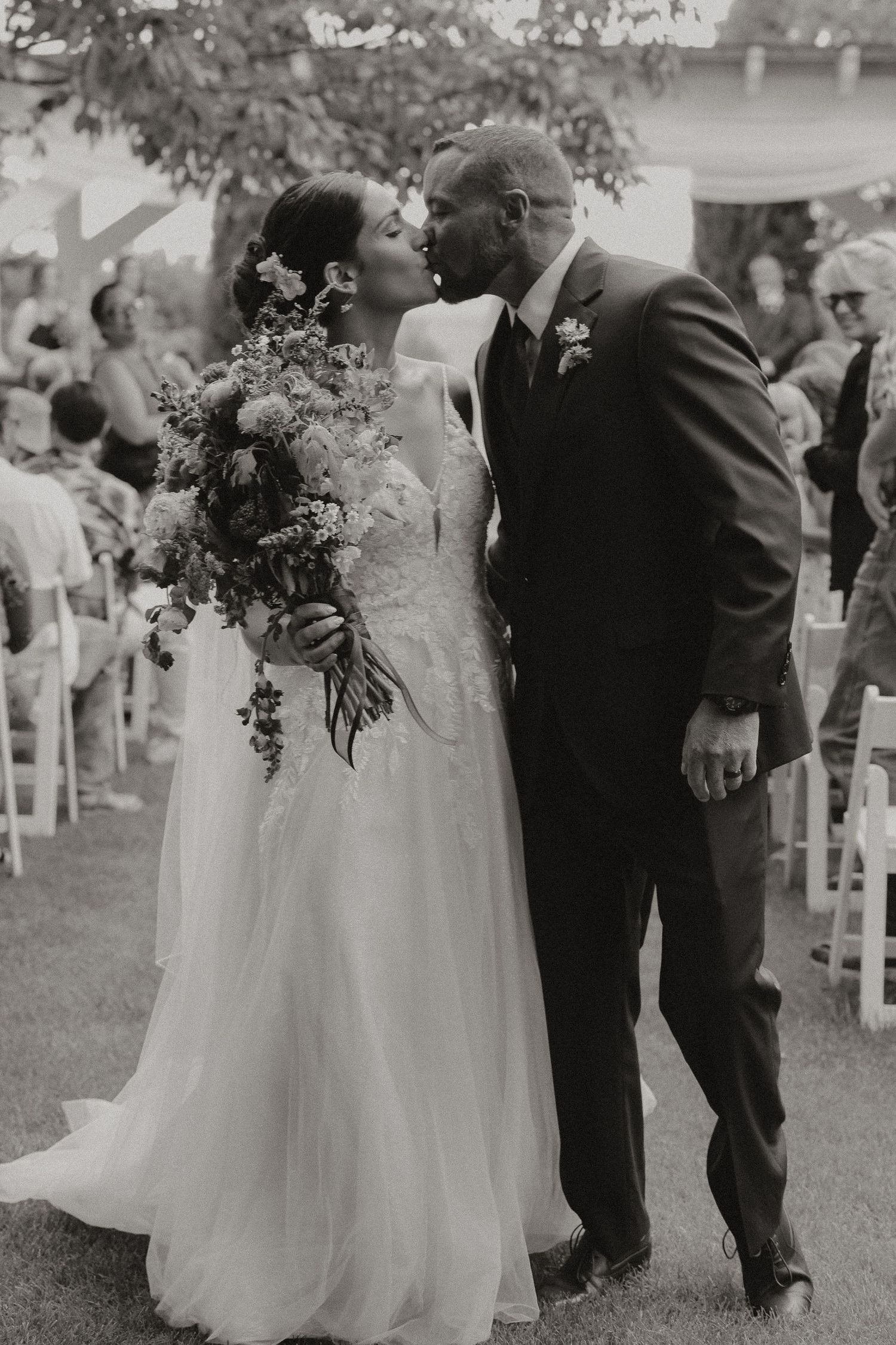 couple kissing in black and white photo on wedding day in the middle of the aisle